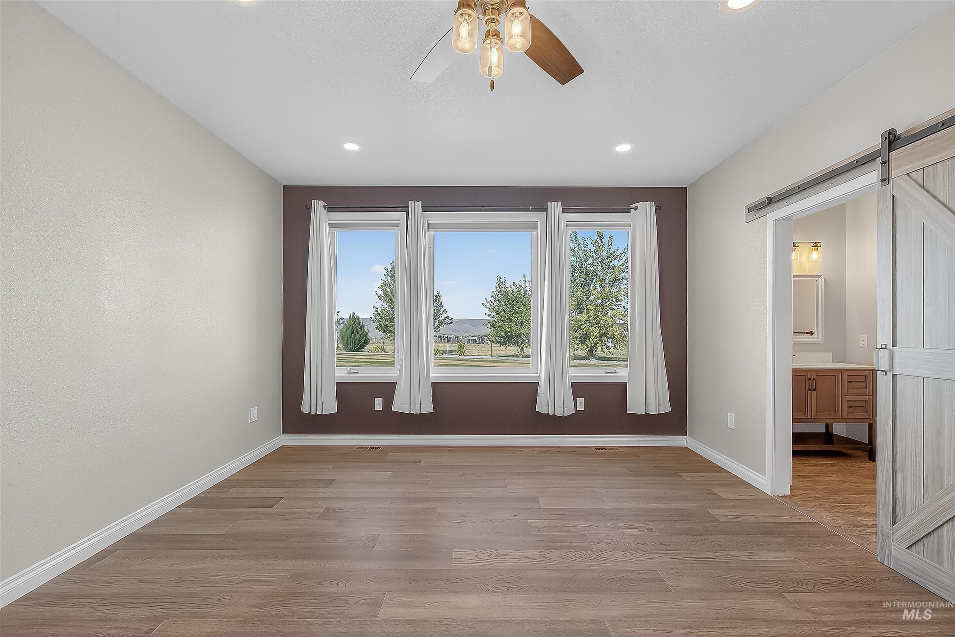 Empty room featuring a barn door, light wood finished floors, plenty of natural light, and recessed lighting