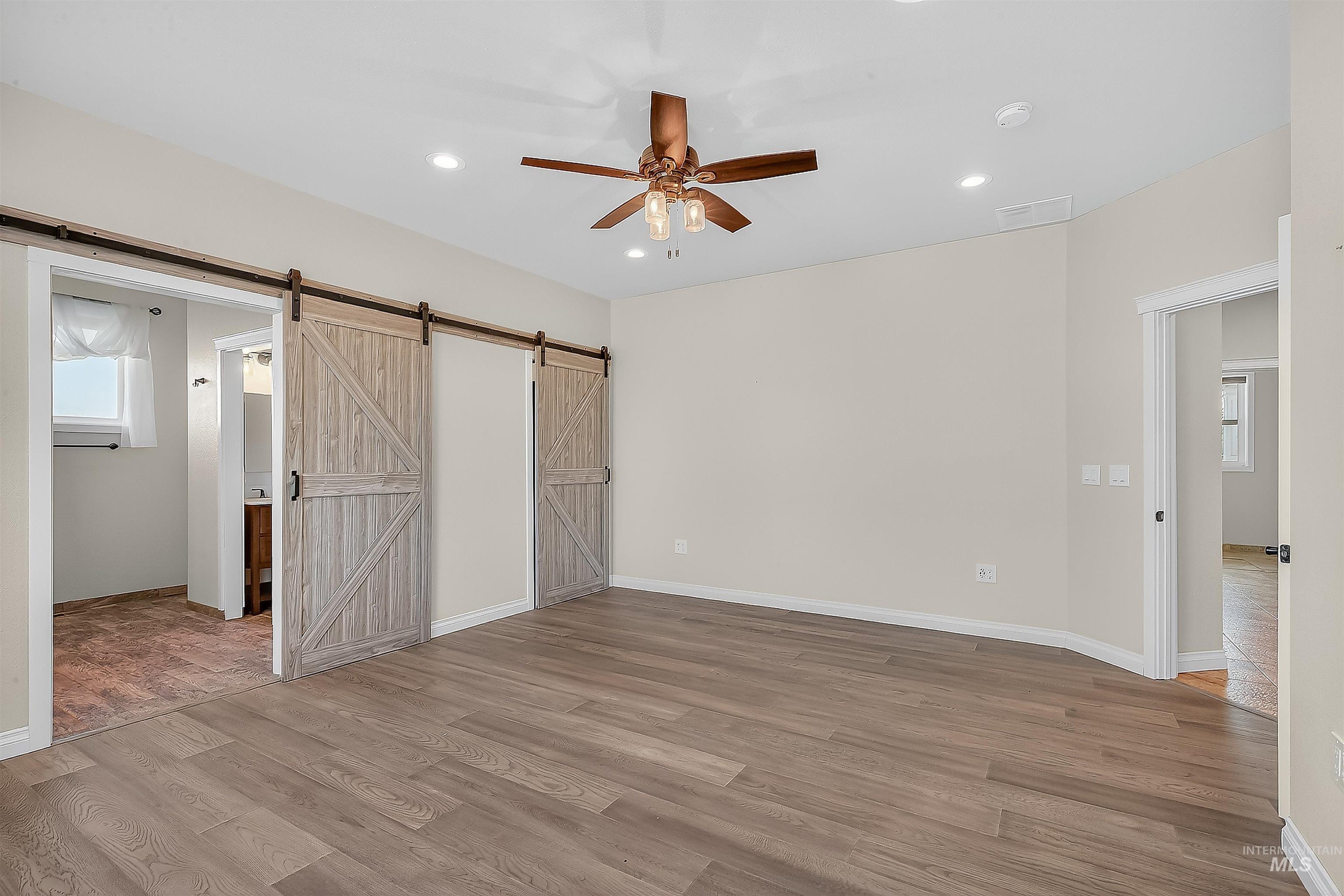 Unfurnished bedroom featuring multiple windows, light wood-style flooring, recessed lighting, a ceiling fan, and a barn door
