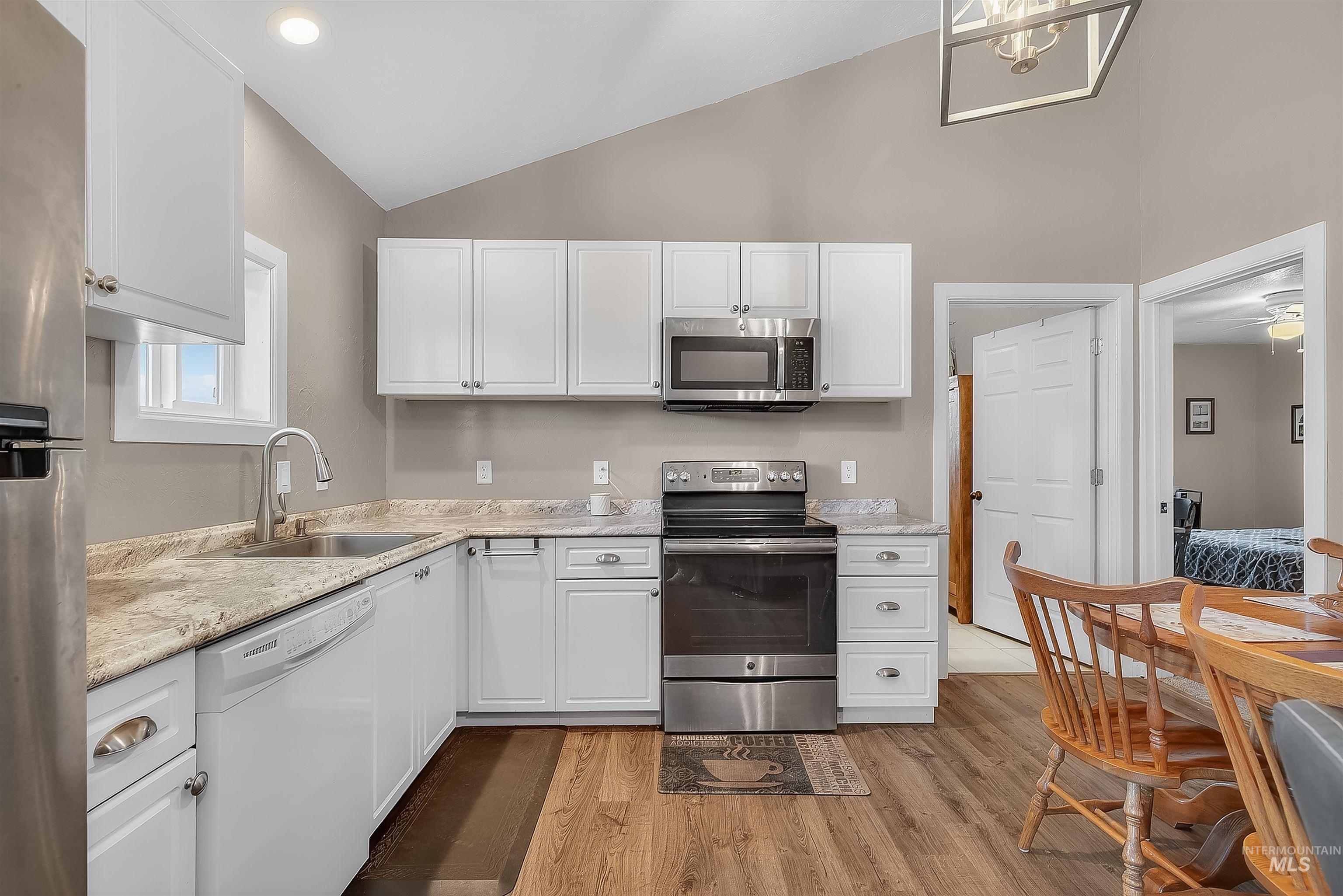 Kitchen featuring lofted ceiling, appliances with stainless steel finishes, white cabinets, light wood-style floors, and recessed lighting