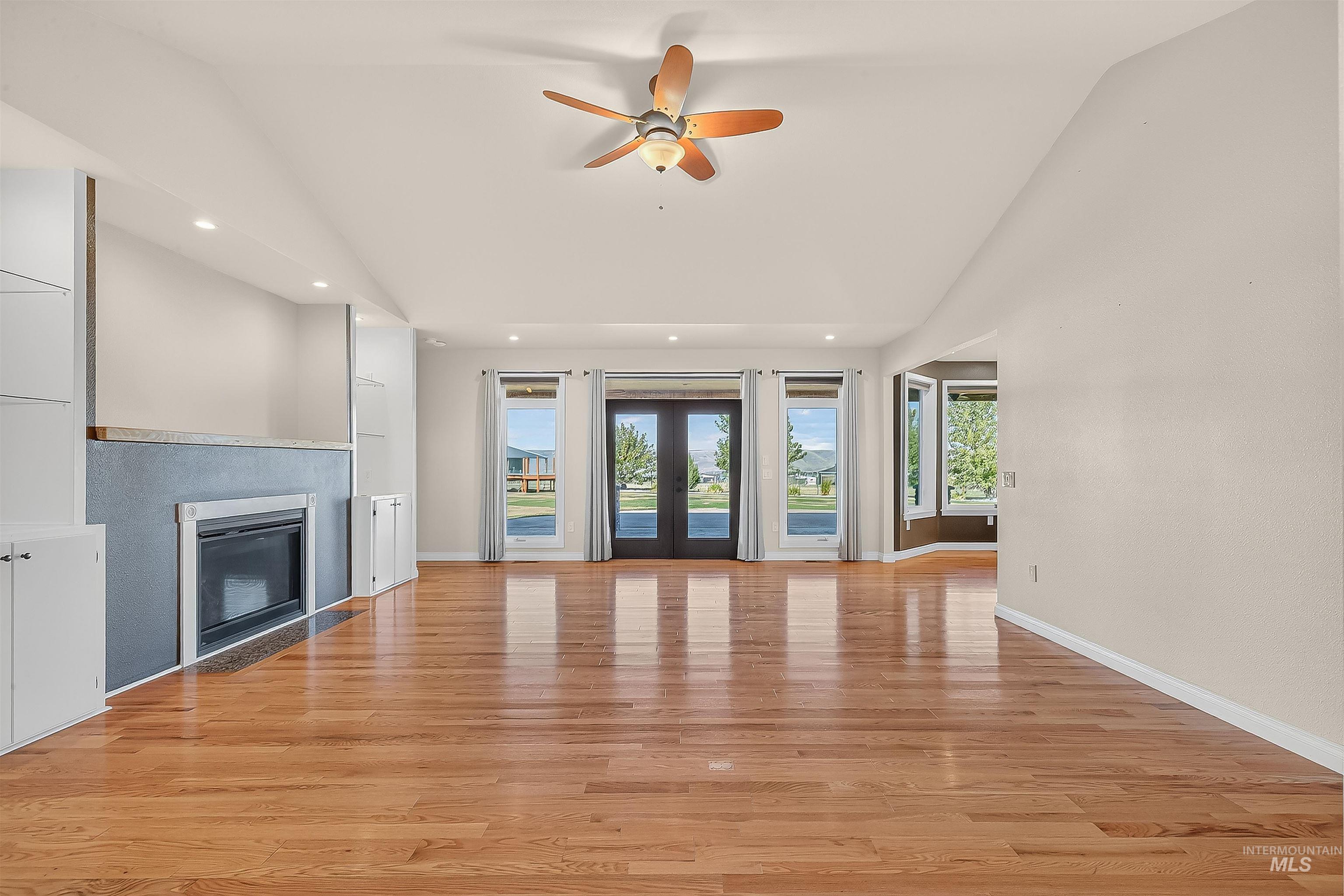 Unfurnished living room featuring healthy amount of natural light, light wood-style flooring, a glass covered fireplace, french doors, and recessed lighting