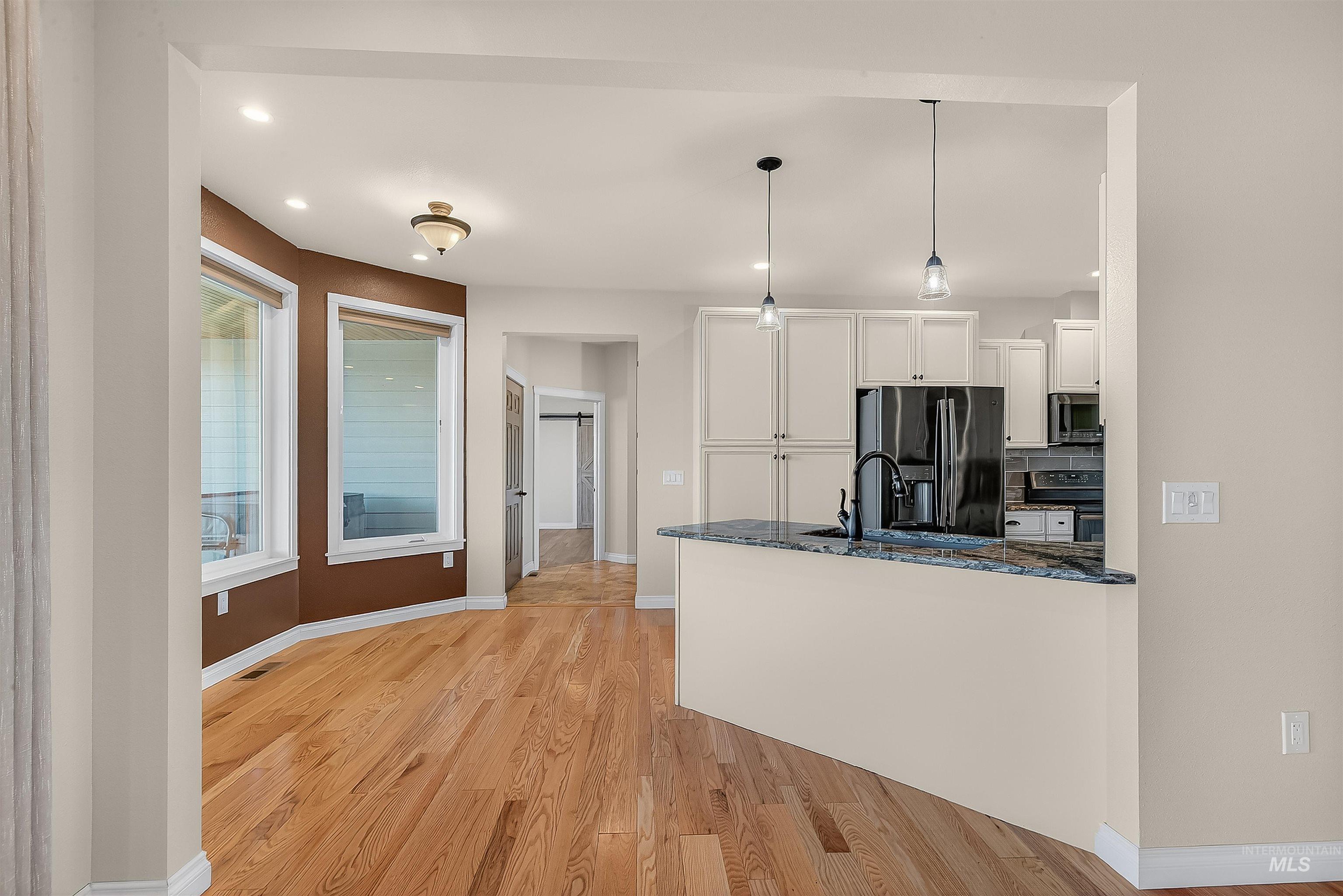 Kitchen featuring decorative light fixtures, white cabinetry, black fridge with ice dispenser, light wood-style floors, and a peninsula
