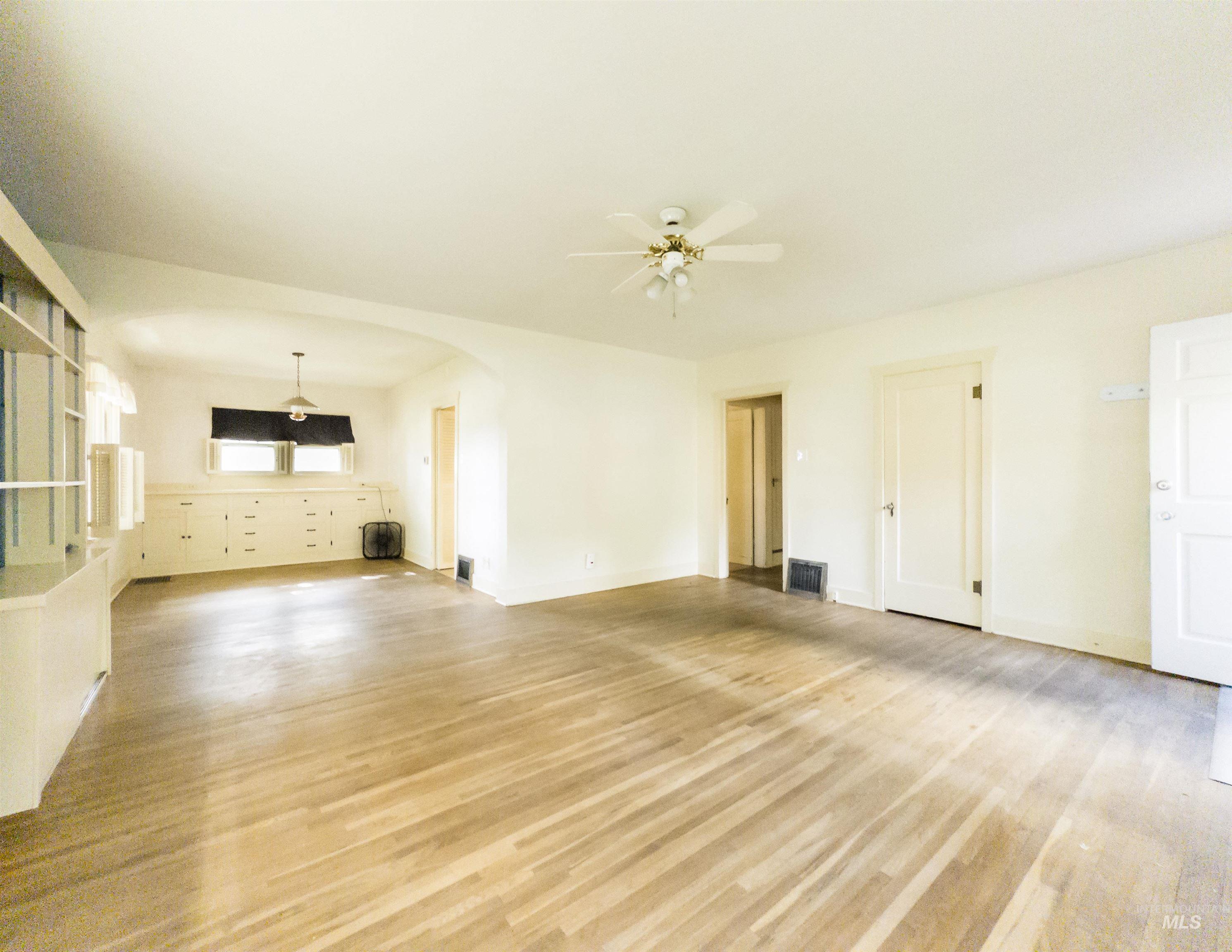 Unfurnished living room with light wood finished floors, arched walkways, and a ceiling fan