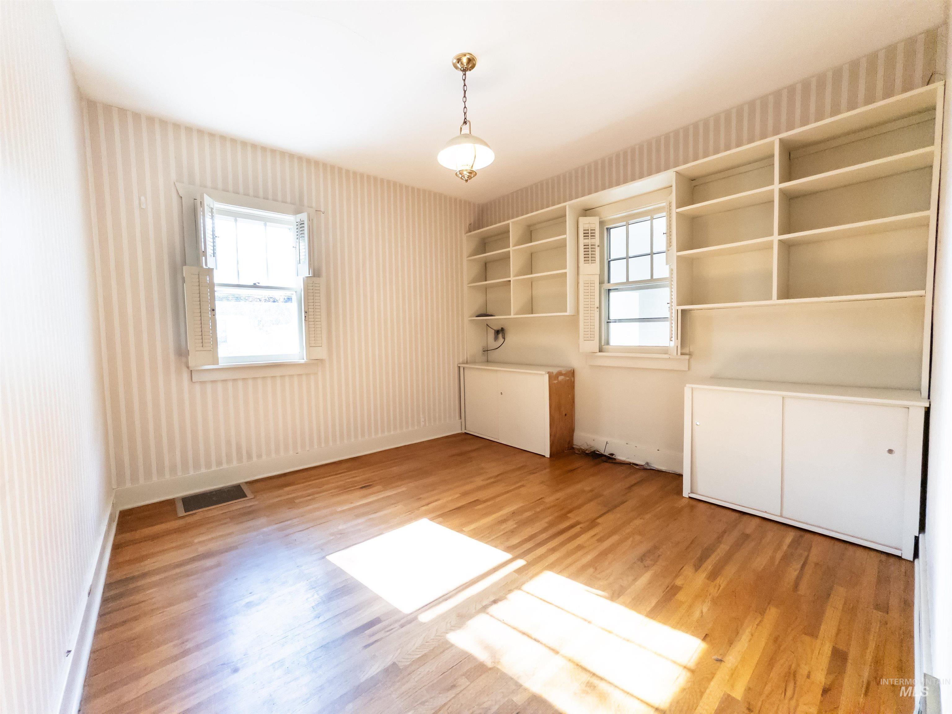 Unfurnished bedroom featuring multiple windows, light wood-style flooring, and wallpapered walls