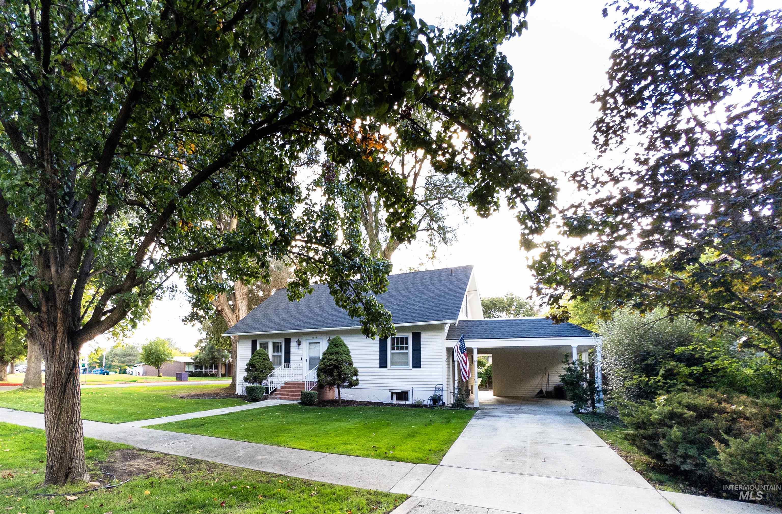 View of front facade with driveway, an attached carport, a front lawn, roof with shingles, and entry steps