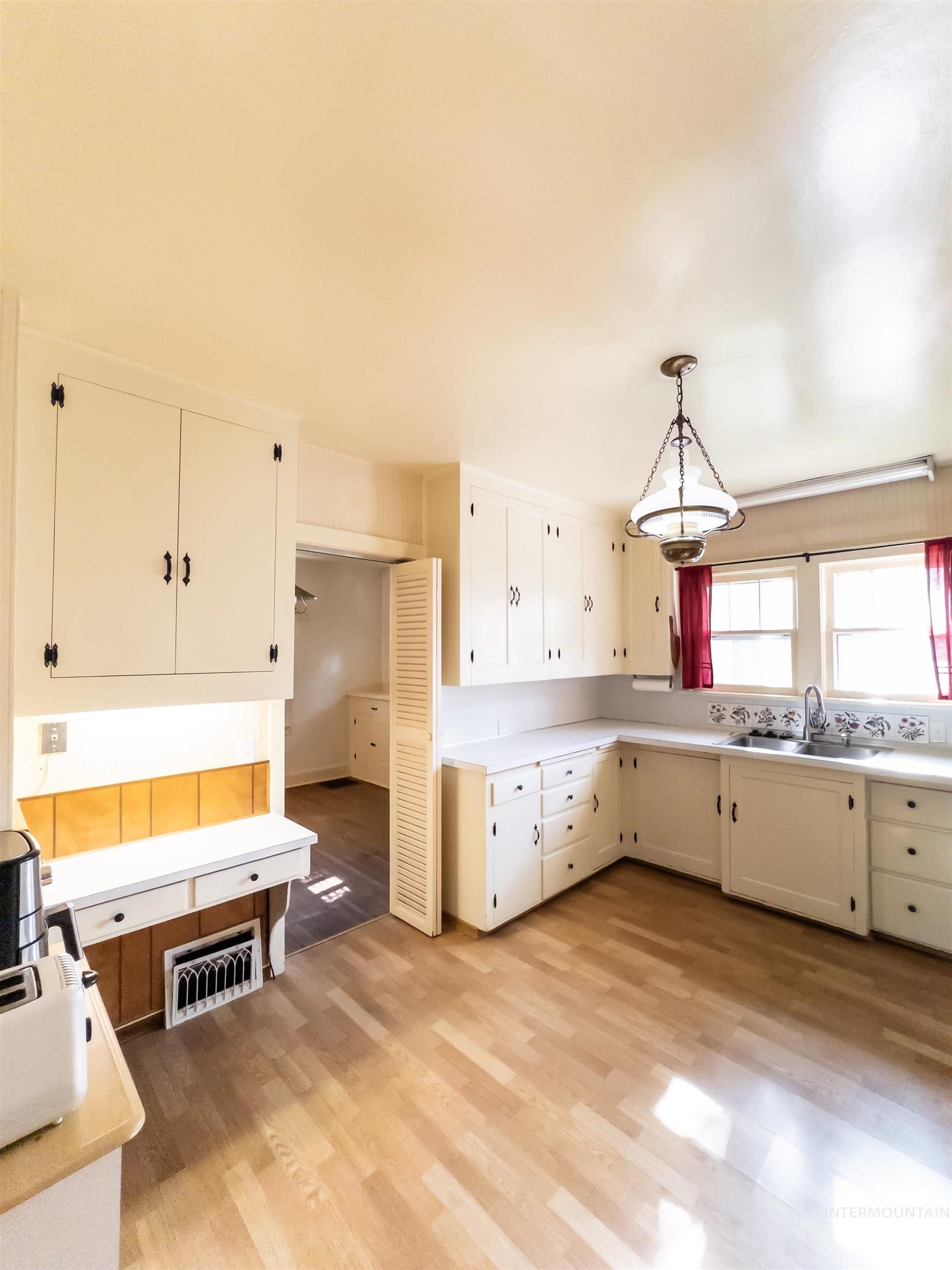 Kitchen featuring light countertops, light wood-style floors, a desk, white cabinets, and decorative light fixtures