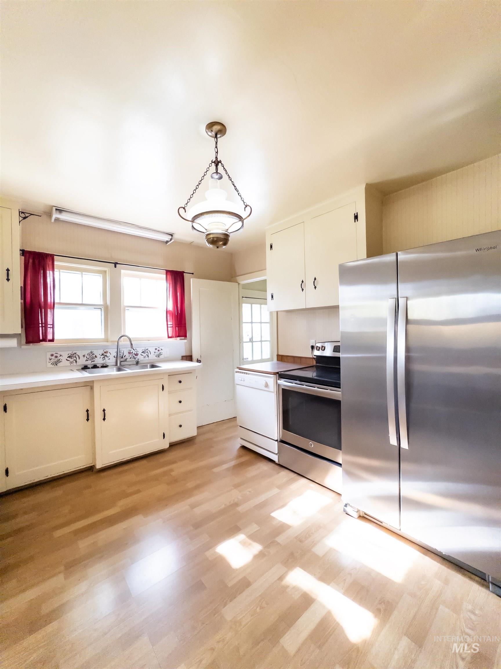 Kitchen featuring appliances with stainless steel finishes, hanging light fixtures, light wood finished floors, and white cabinetry