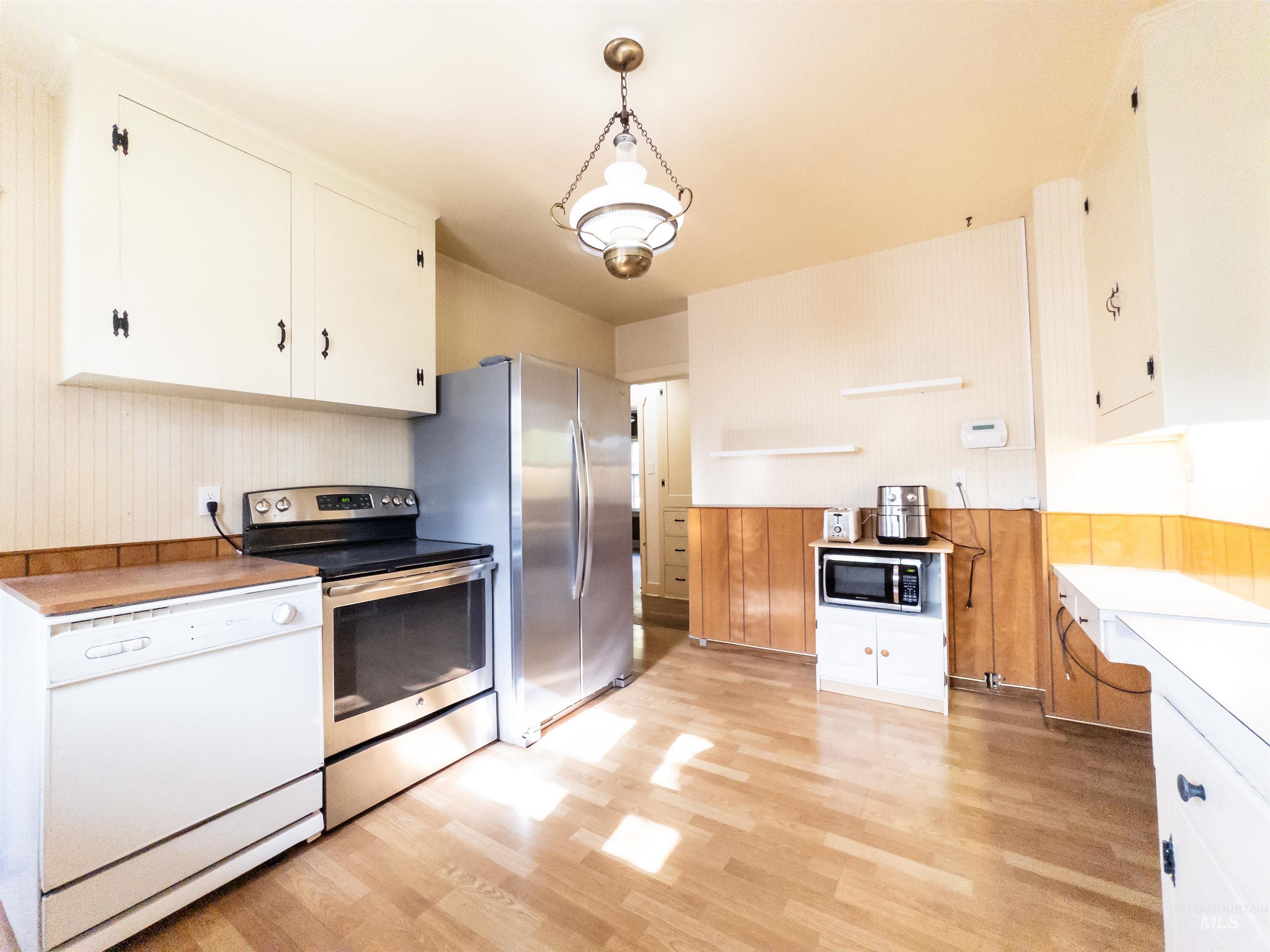 Kitchen with white cabinets, appliances with stainless steel finishes, light countertops, hanging light fixtures, and brown cabinetry