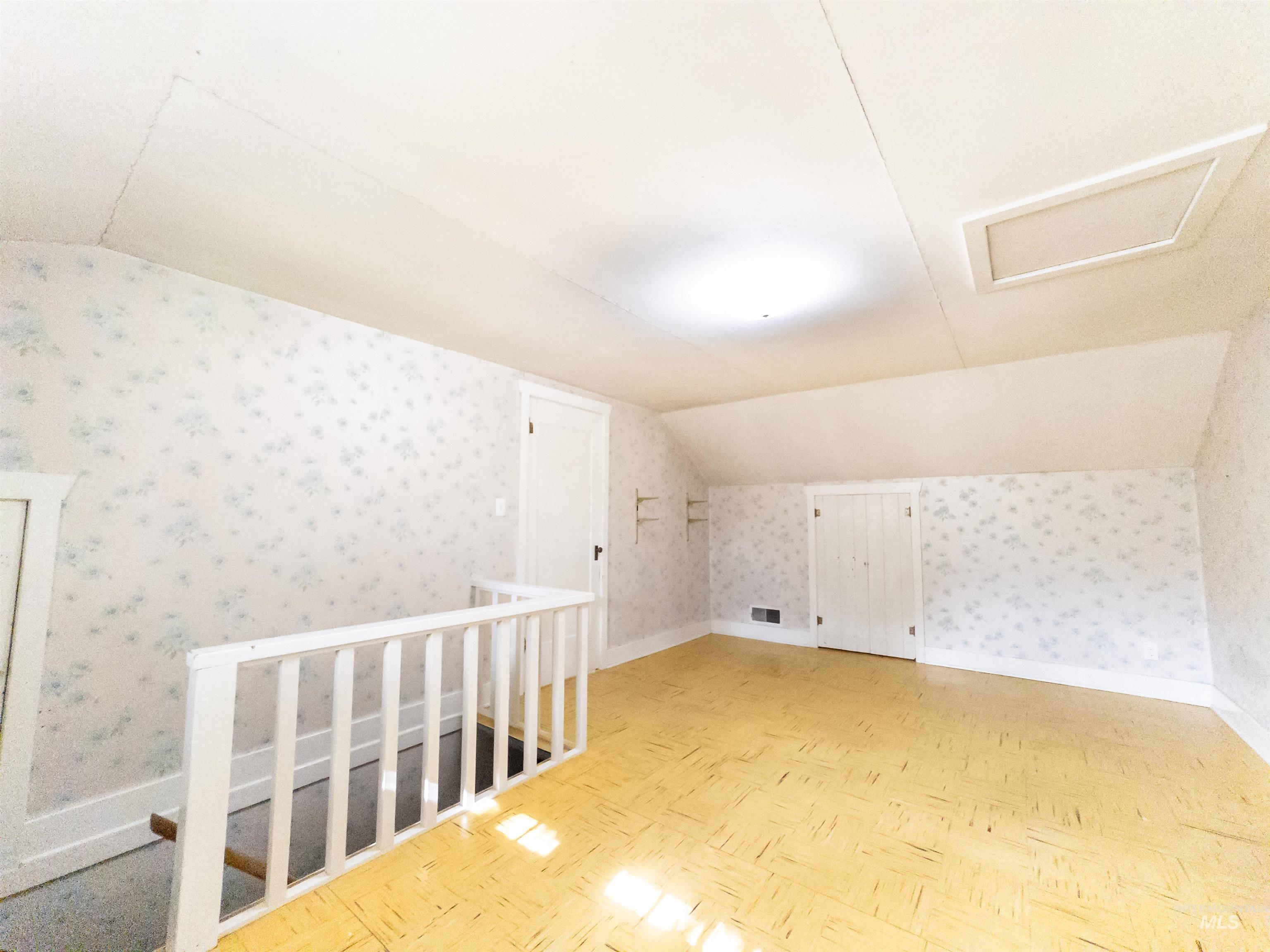 Additional living space with vaulted ceiling, attic access, and wallpapered walls