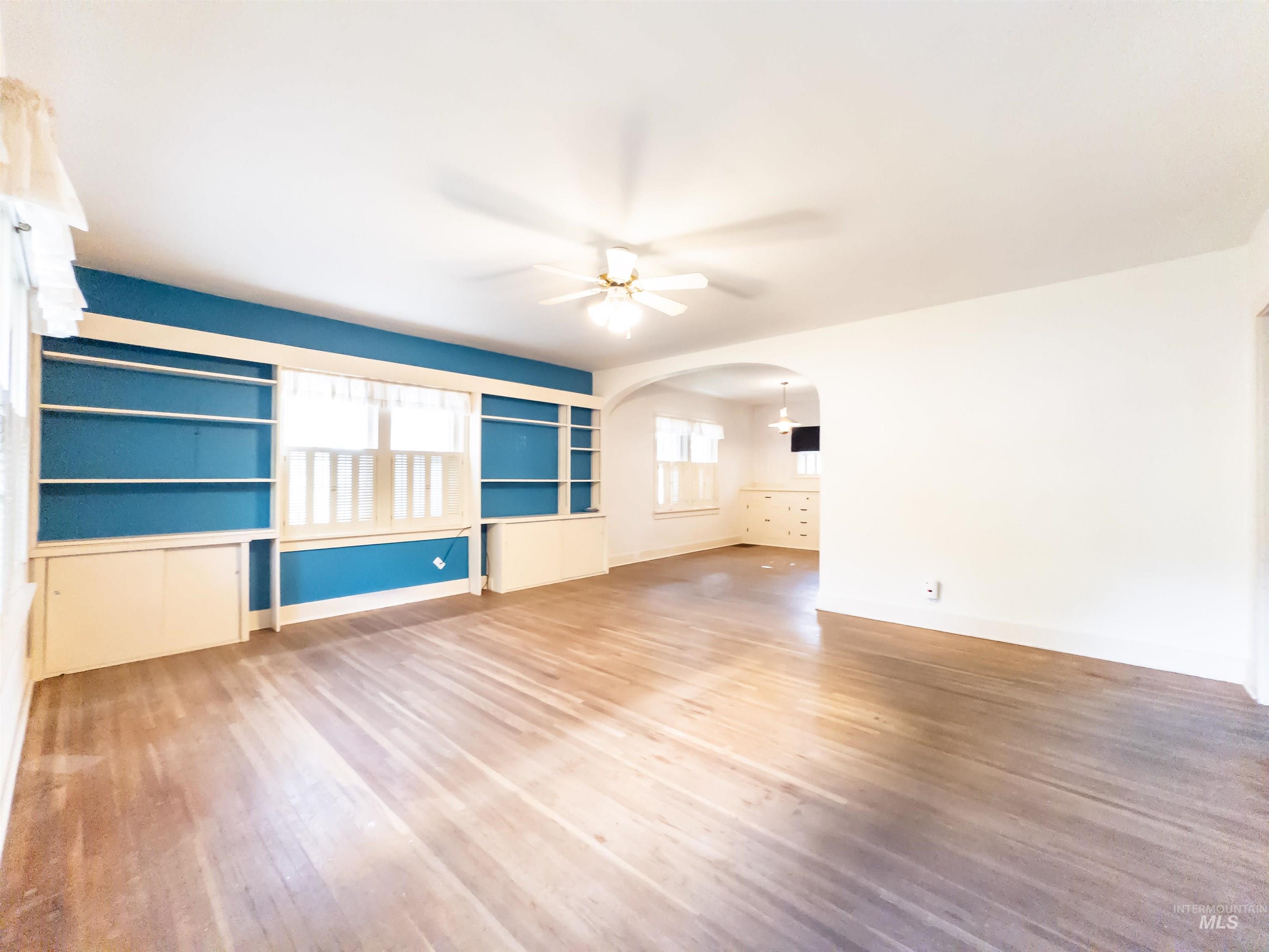 Unfurnished living room with light wood-style flooring, built in shelves, a ceiling fan, and arched walkways