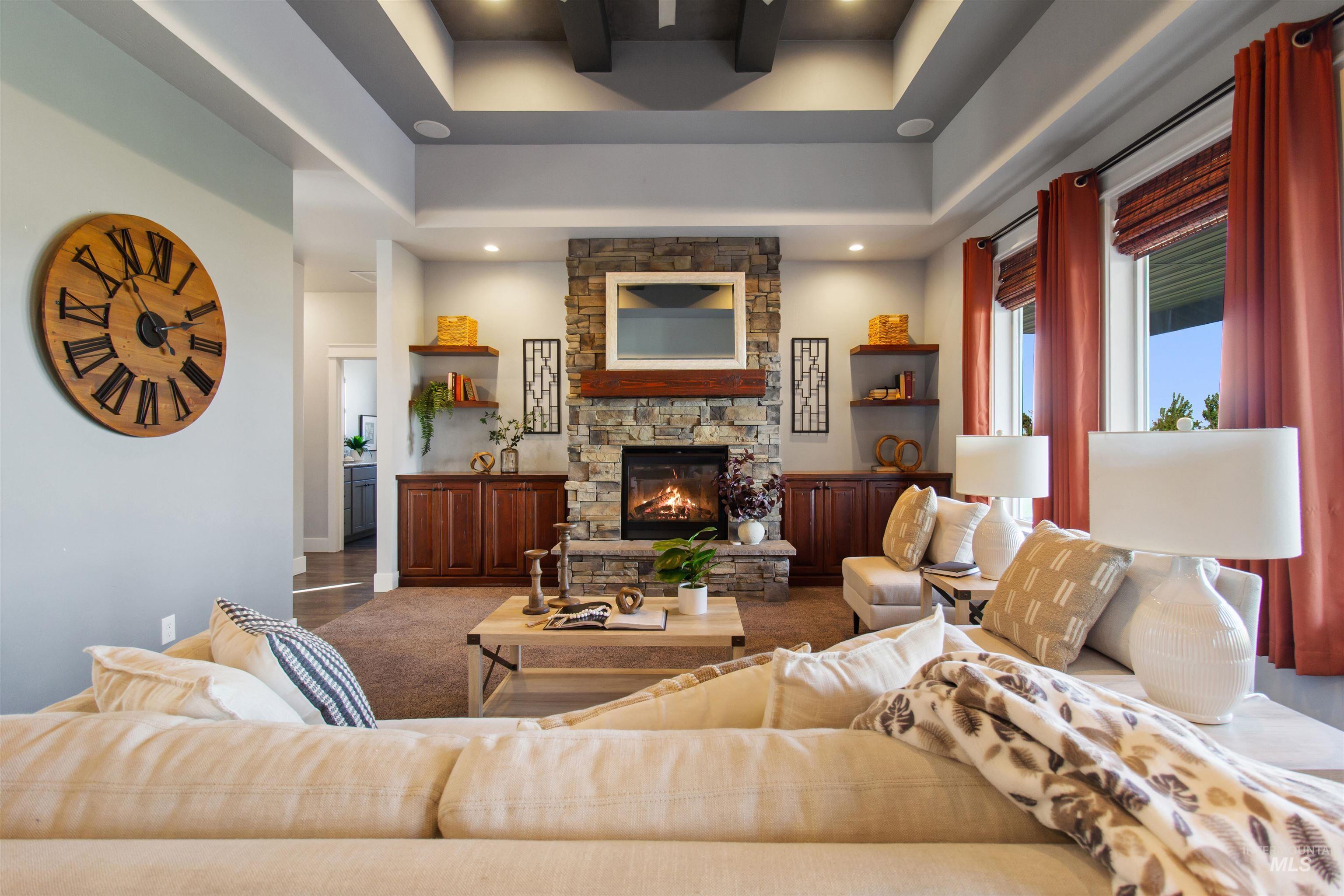 Carpeted living area with a stone fireplace and a tray ceiling