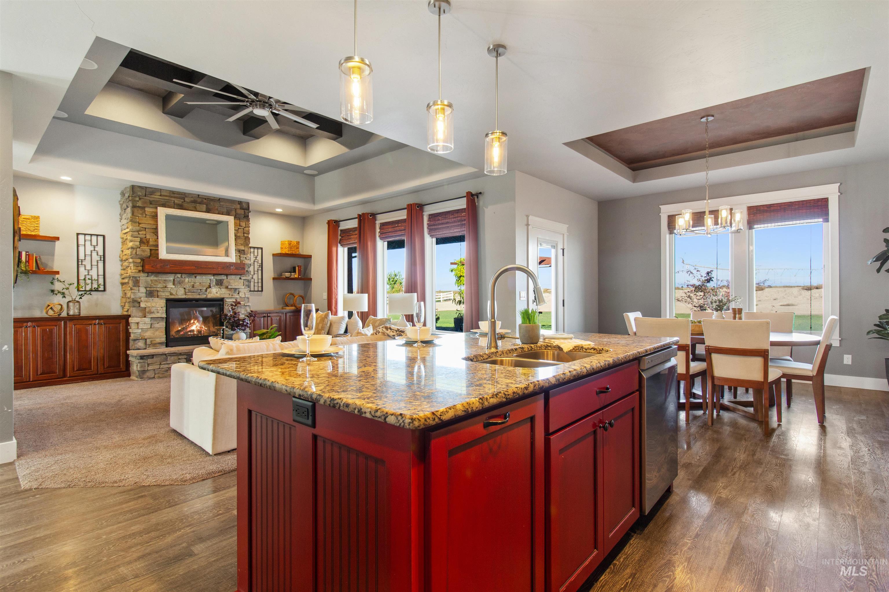 Kitchen with a tray ceiling, dark brown cabinets, light stone countertops, pendant lighting, and dark wood-style flooring