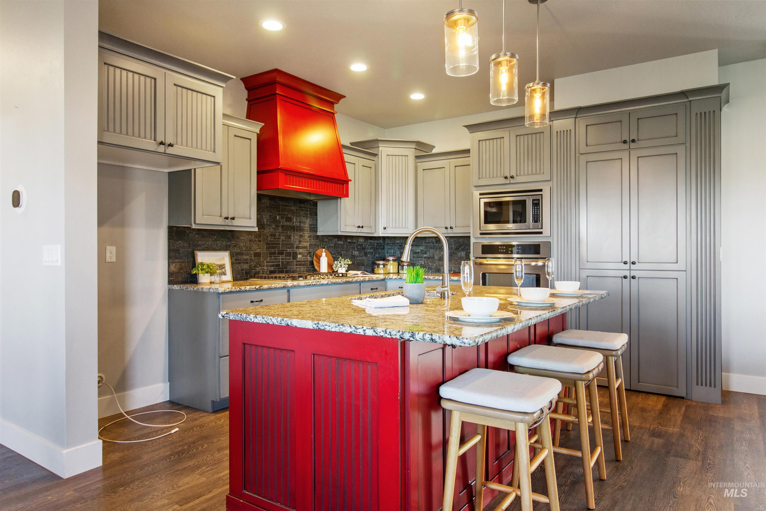 Kitchen featuring light stone counters, decorative backsplash, appliances with stainless steel finishes, hanging light fixtures, and a kitchen bar