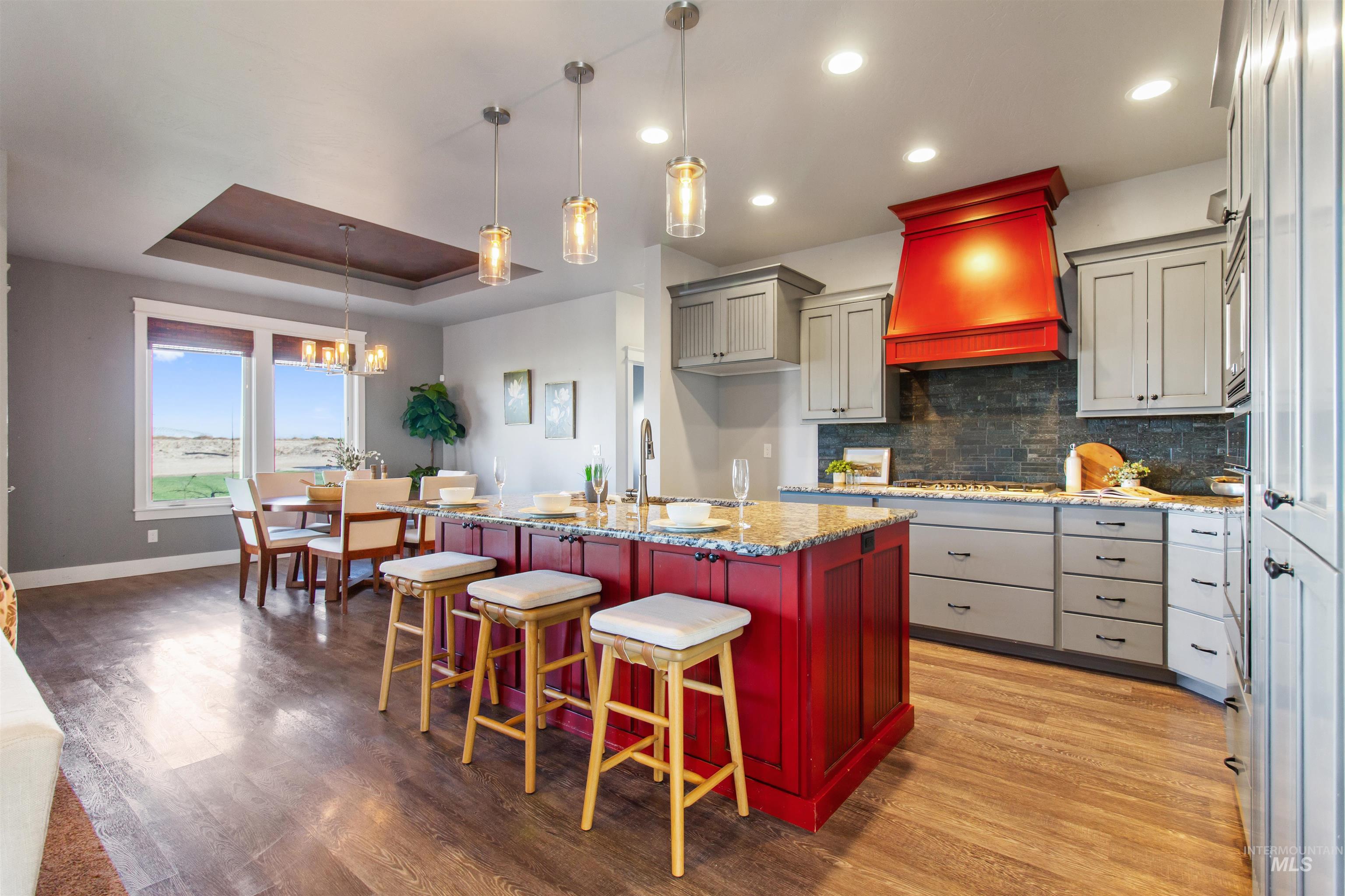 Kitchen with a raised ceiling, backsplash, reddish brown cabinets, custom range hood, and light stone countertops