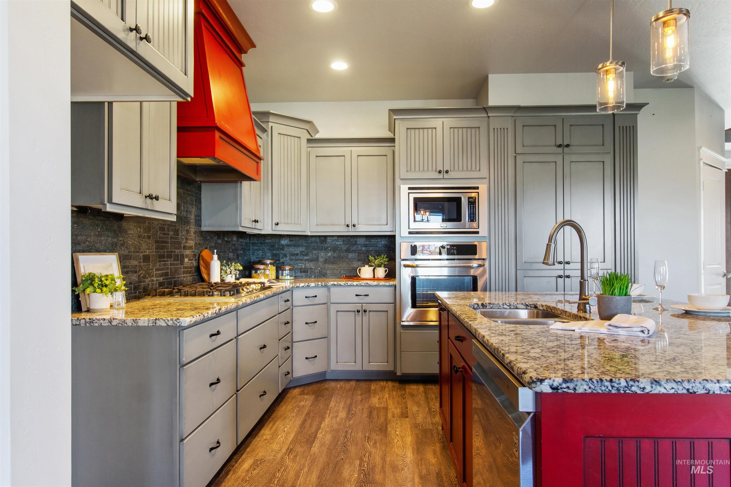 Kitchen featuring stainless steel appliances, dark wood-style flooring, hanging light fixtures, decorative backsplash, and light stone counters