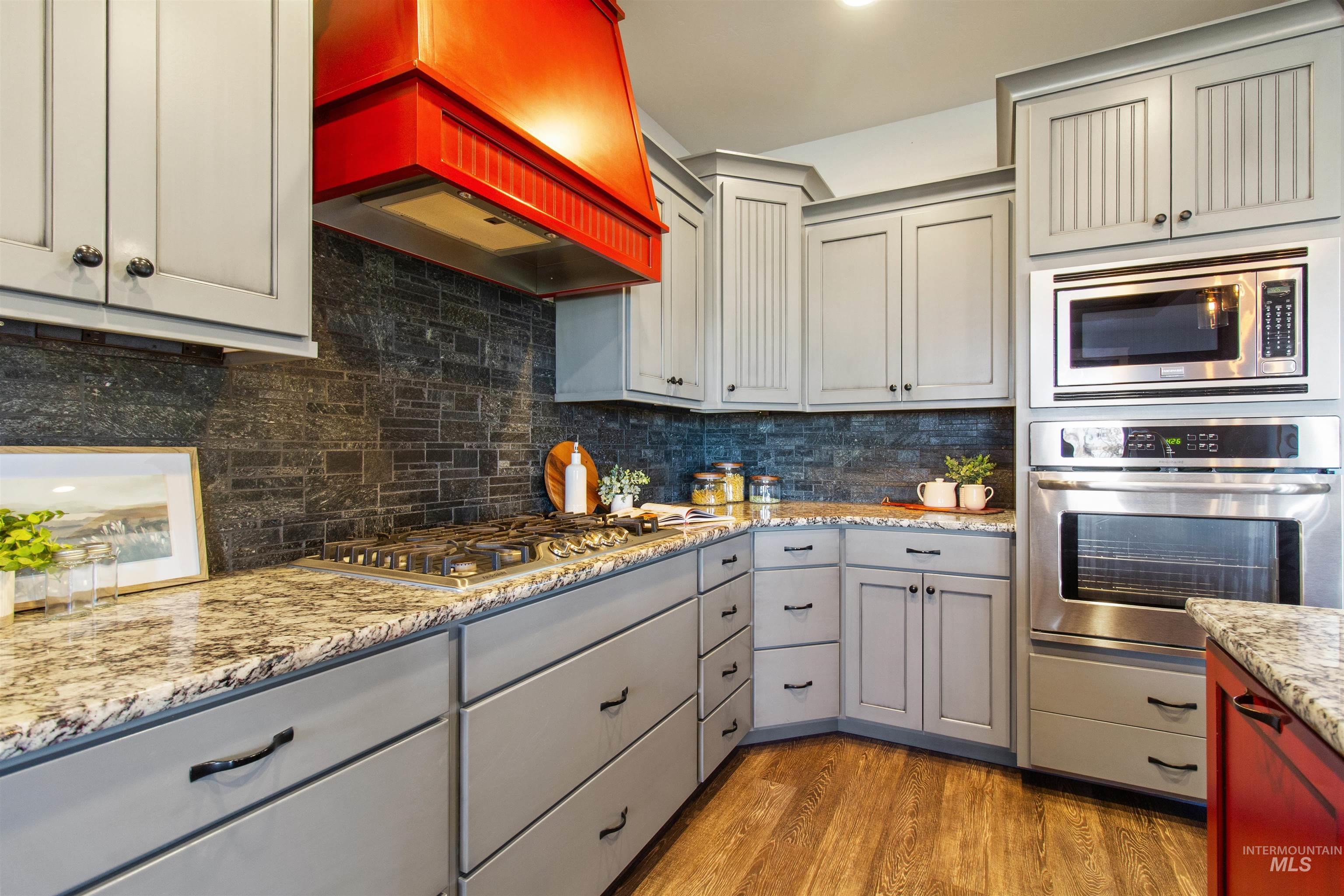 Kitchen with gray cabinetry, appliances with stainless steel finishes, premium range hood, light wood finished floors, and backsplash