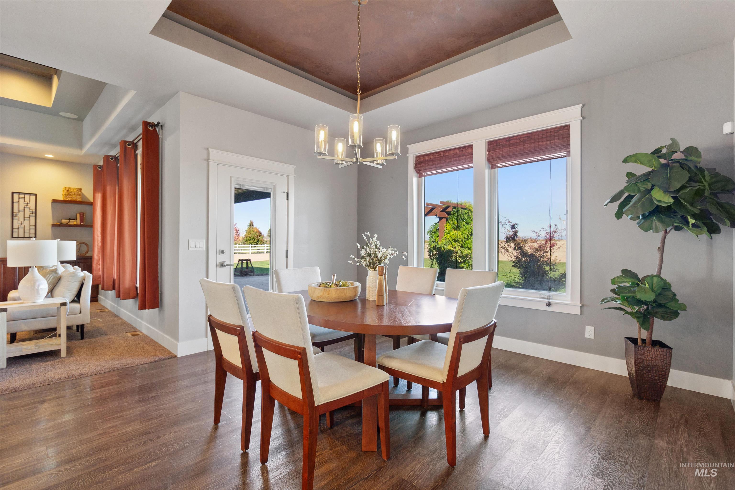 Dining area with a tray ceiling, dark wood-type flooring, plenty of natural light, and a chandelier