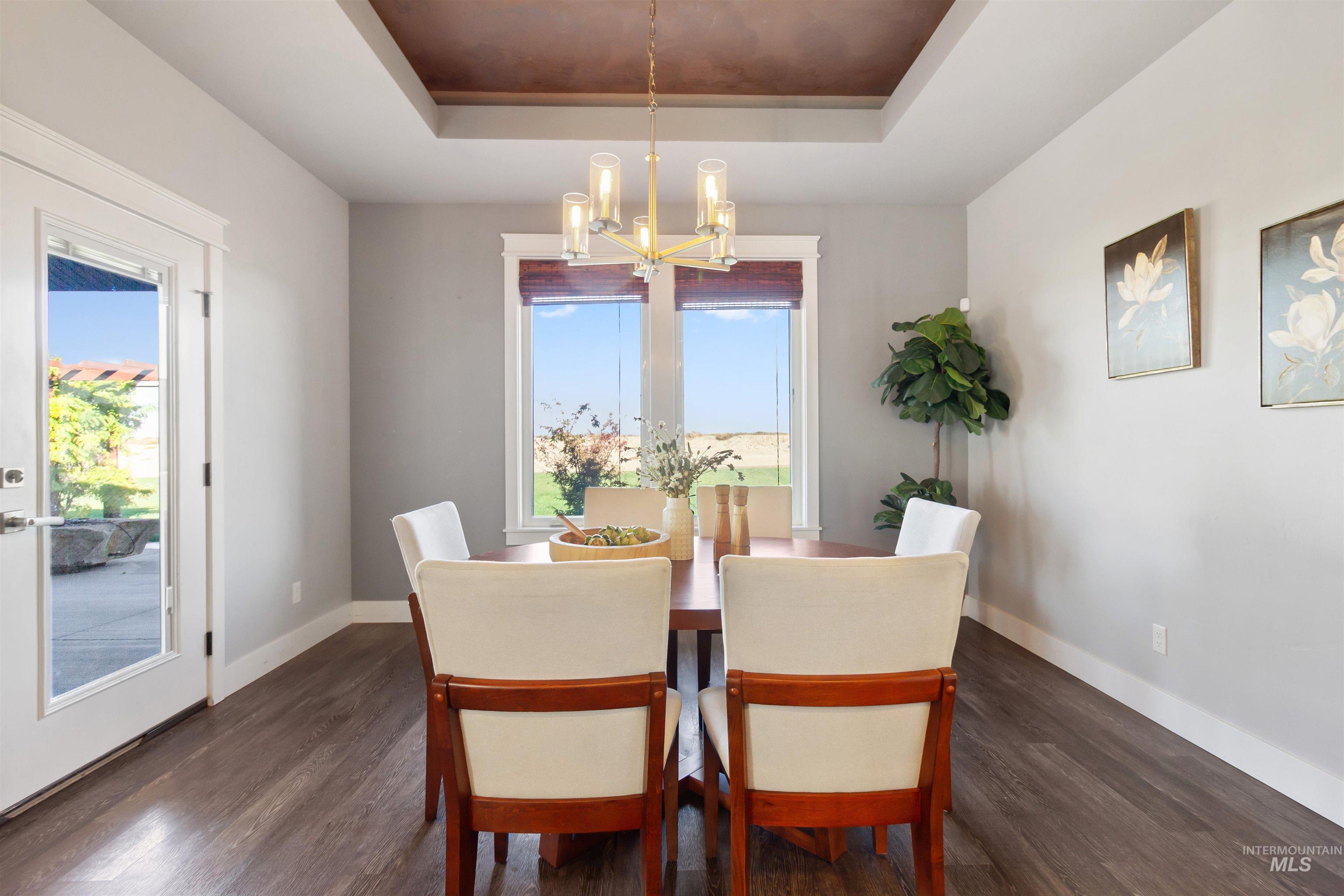 Dining space featuring a raised ceiling, dark wood-style floors, and a chandelier