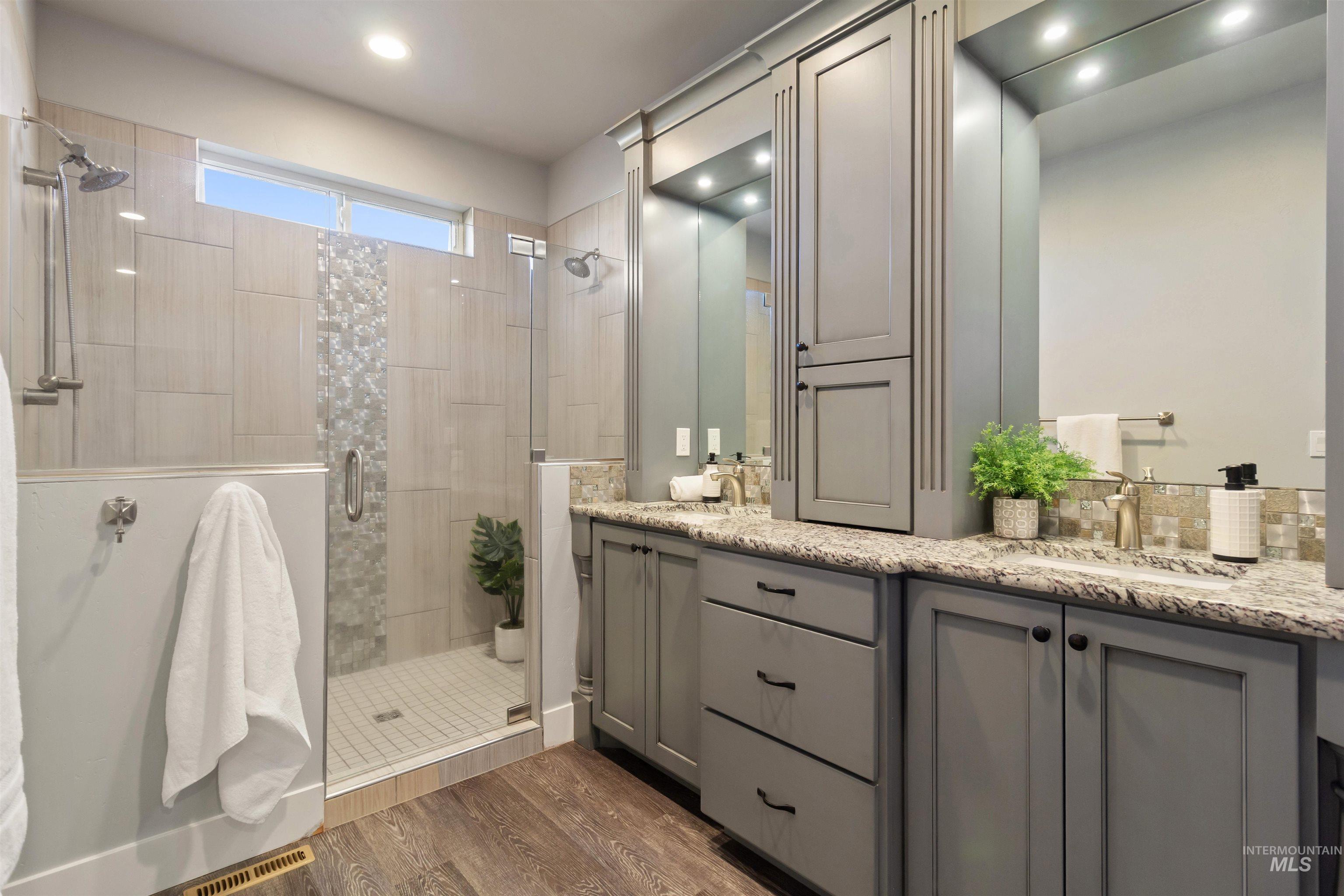 Bathroom with double vanity, dark wood-type flooring, a stall shower, and recessed lighting