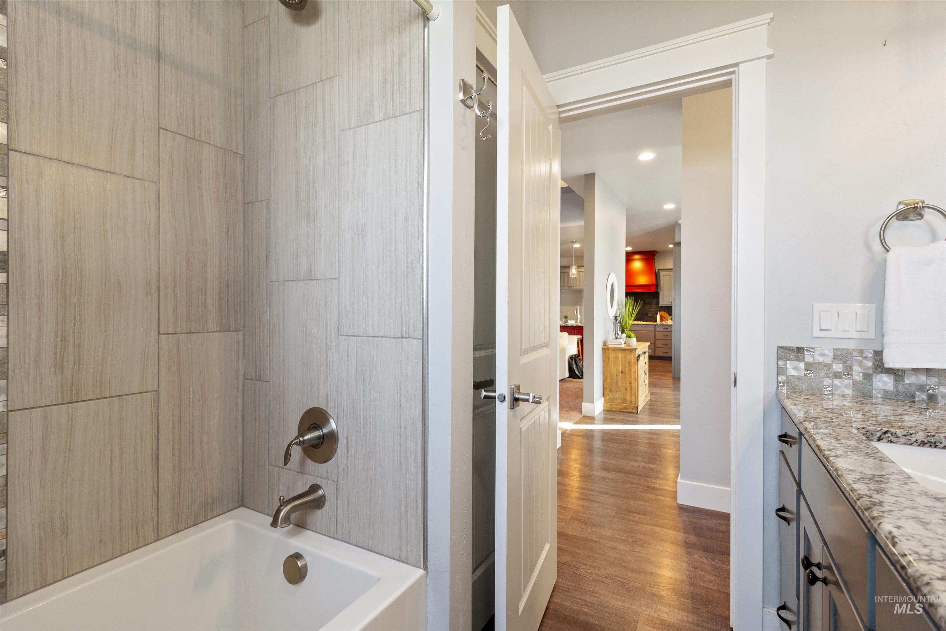 Bathroom with vanity, dark wood-style floors, shower / bath combination, and decorative backsplash