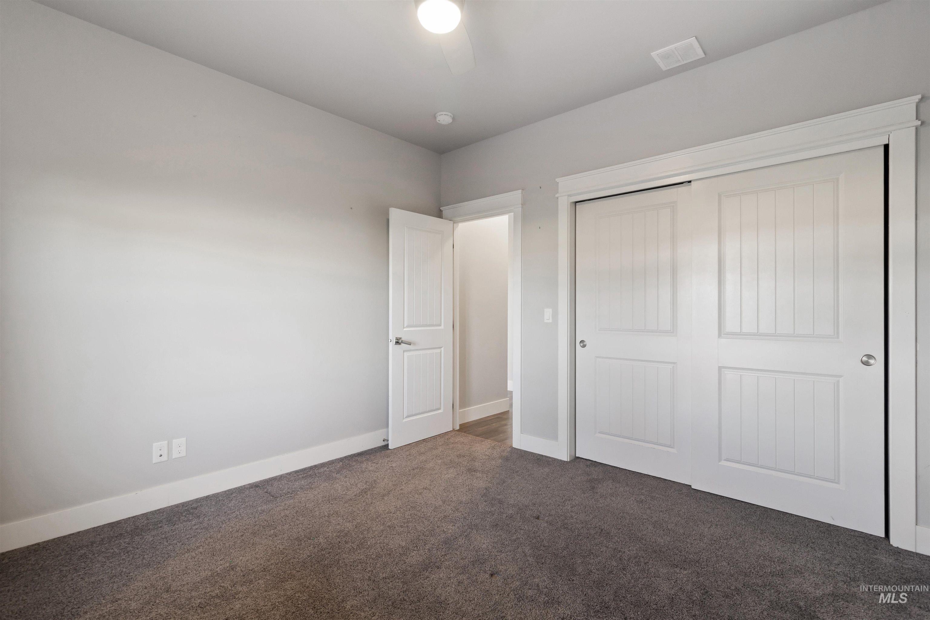 Unfurnished bedroom with dark colored carpet, a closet, and ceiling fan
