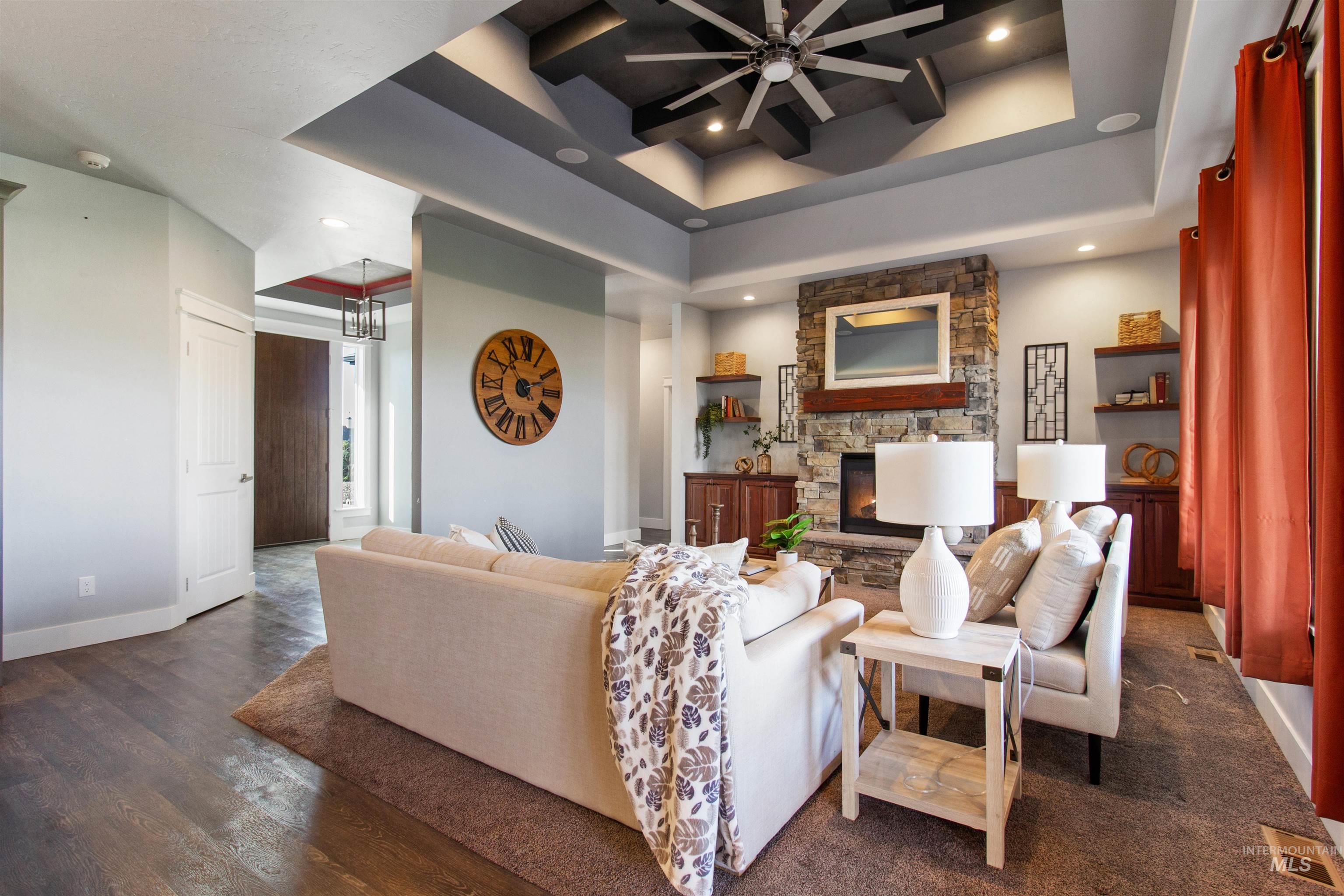 Living area featuring a tray ceiling, a stone fireplace, recessed lighting, dark wood-style flooring, and a ceiling fan