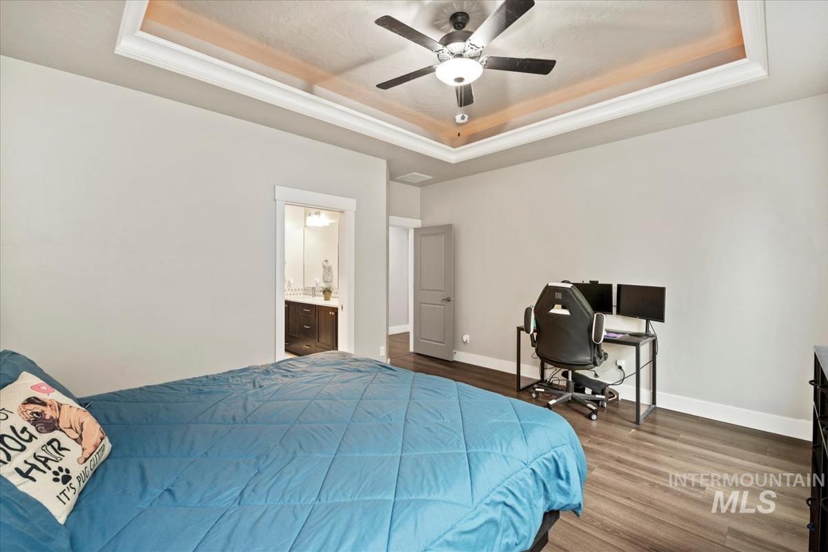 Bedroom featuring a tray ceiling, wood finished floors, ceiling fan, and ensuite bath