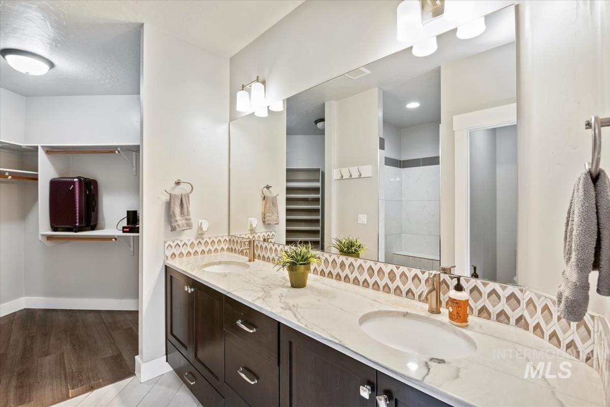 Bathroom with a spacious closet, double vanity, a tile shower, and light wood-style floors