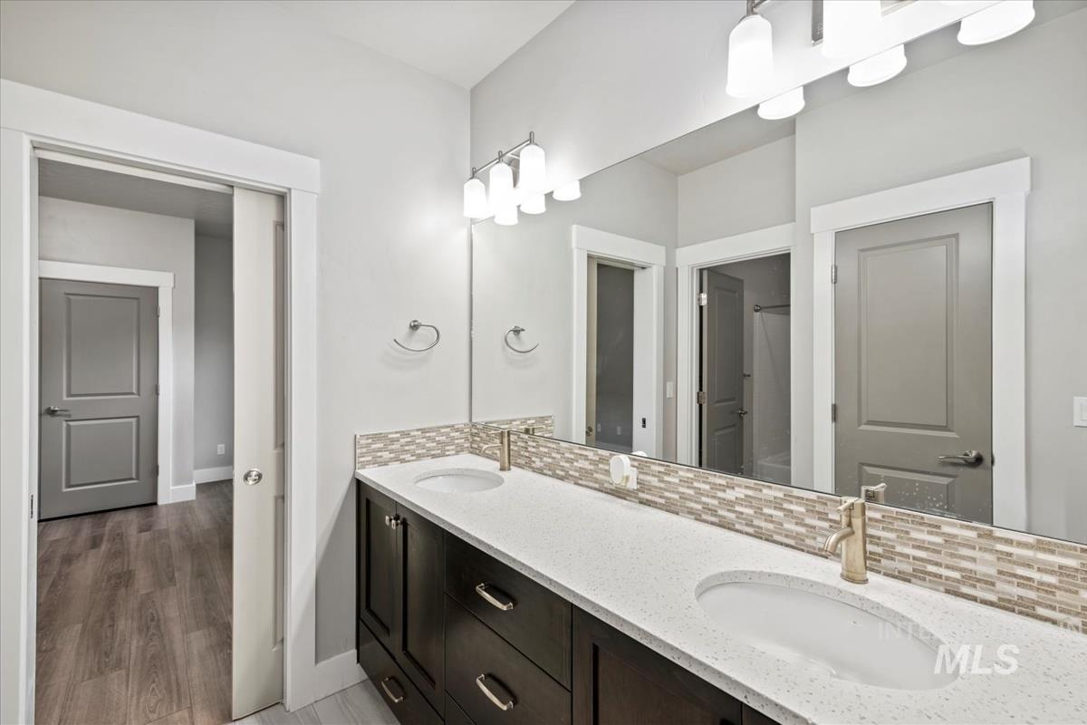 Full bath with tasteful backsplash, double vanity, and light wood-style flooring