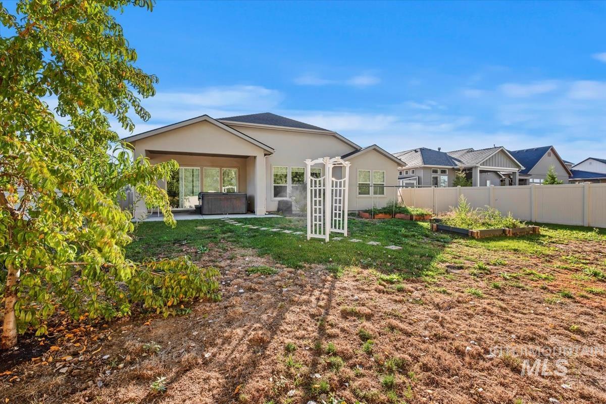 Rear view of house with a patio, a hot tub, stucco siding, a fenced backyard, and a garden