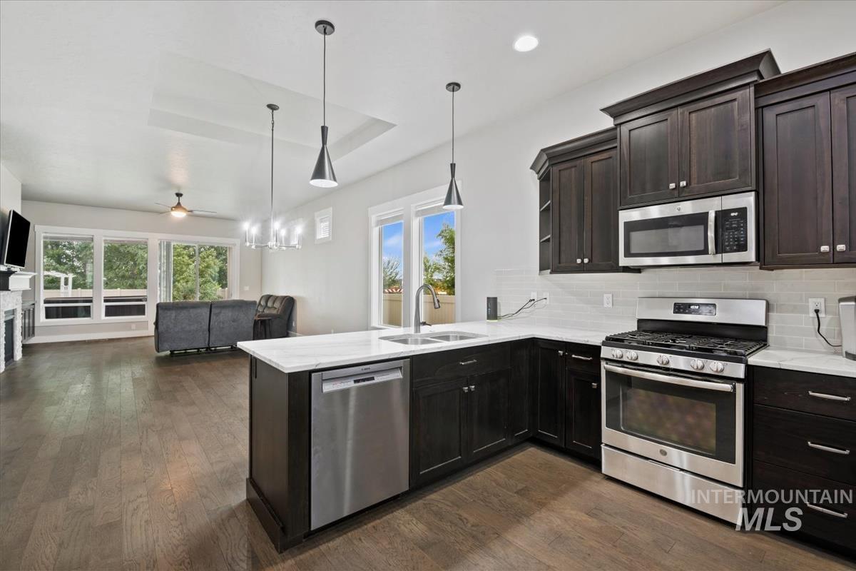 Kitchen with appliances with stainless steel finishes, backsplash, light stone counters, pendant lighting, and recessed lighting