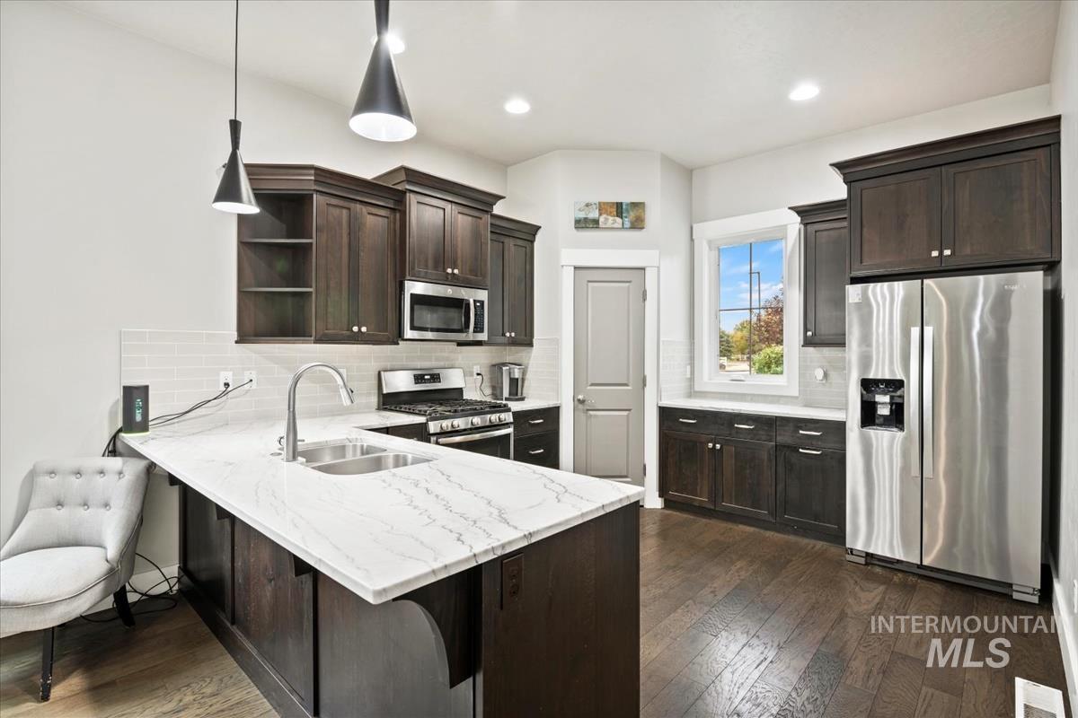 Kitchen featuring open shelves, stainless steel appliances, dark brown cabinets, a peninsula, and light stone counters