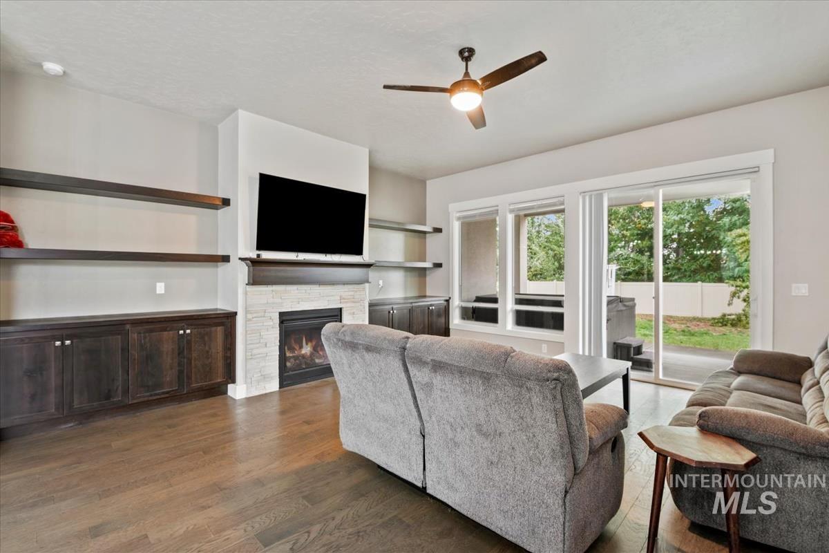 Living room with ceiling fan, dark wood-style flooring, and a fireplace