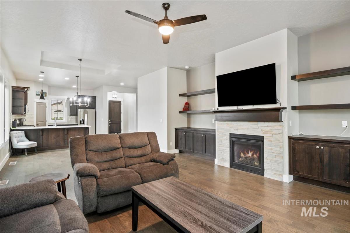 Living room with a chandelier, light wood finished floors, a ceiling fan, a stone fireplace, and recessed lighting