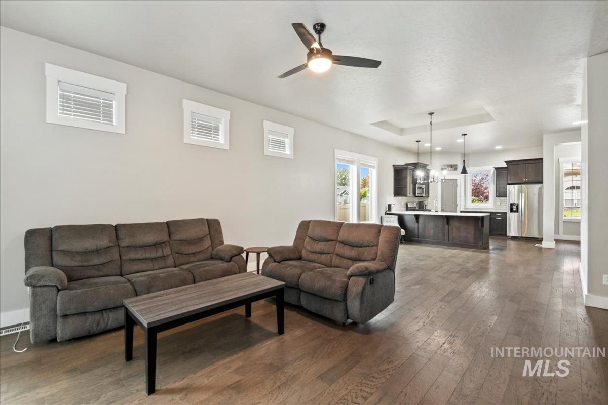 Living room with dark wood-style floors, plenty of natural light, ceiling fan, and a raised ceiling