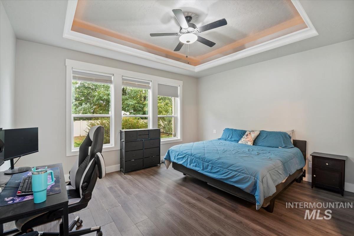 Bedroom with a tray ceiling, wood finished floors, a ceiling fan, and an office area