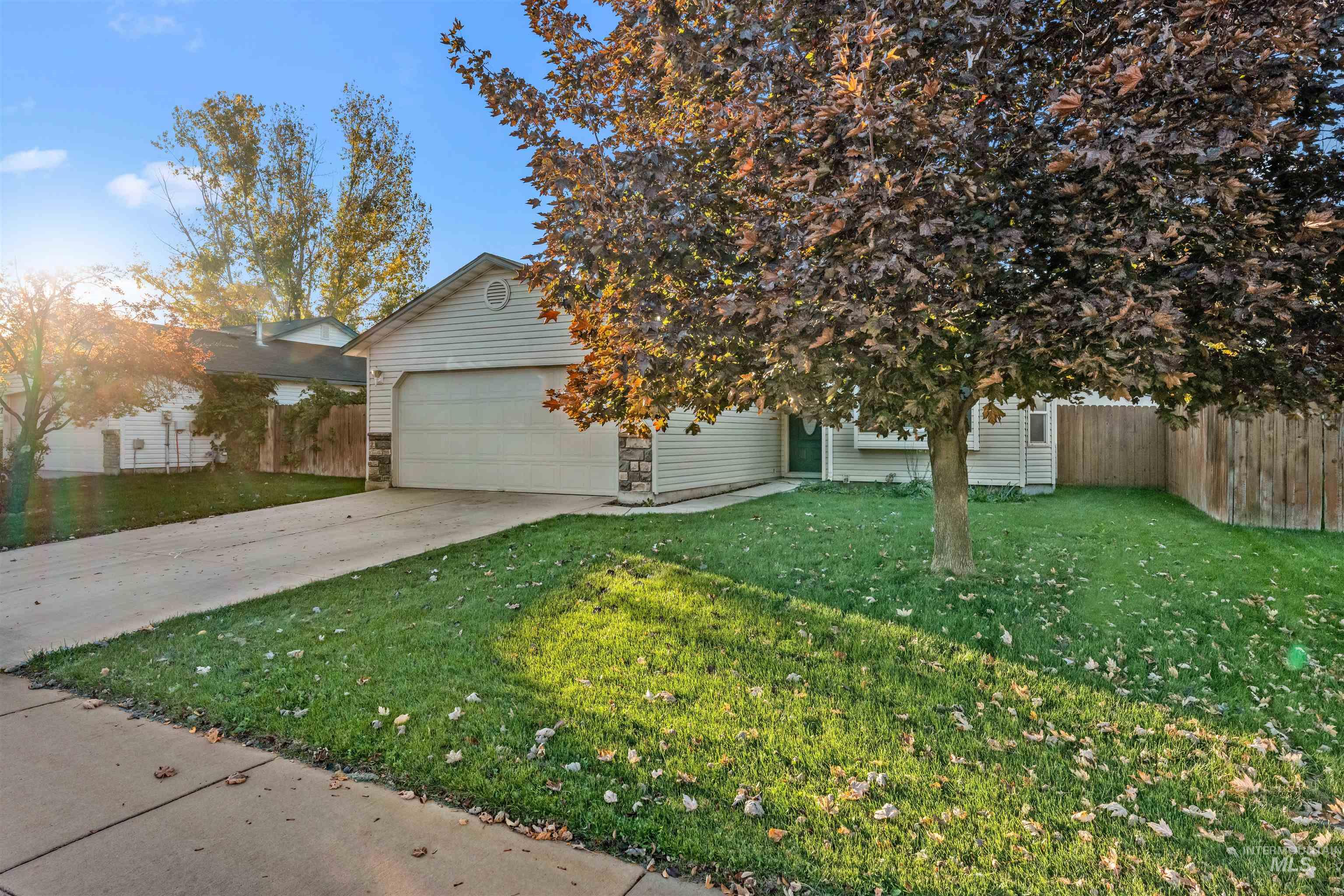 View of property hidden behind natural elements with concrete driveway, an attached garage, and stone siding