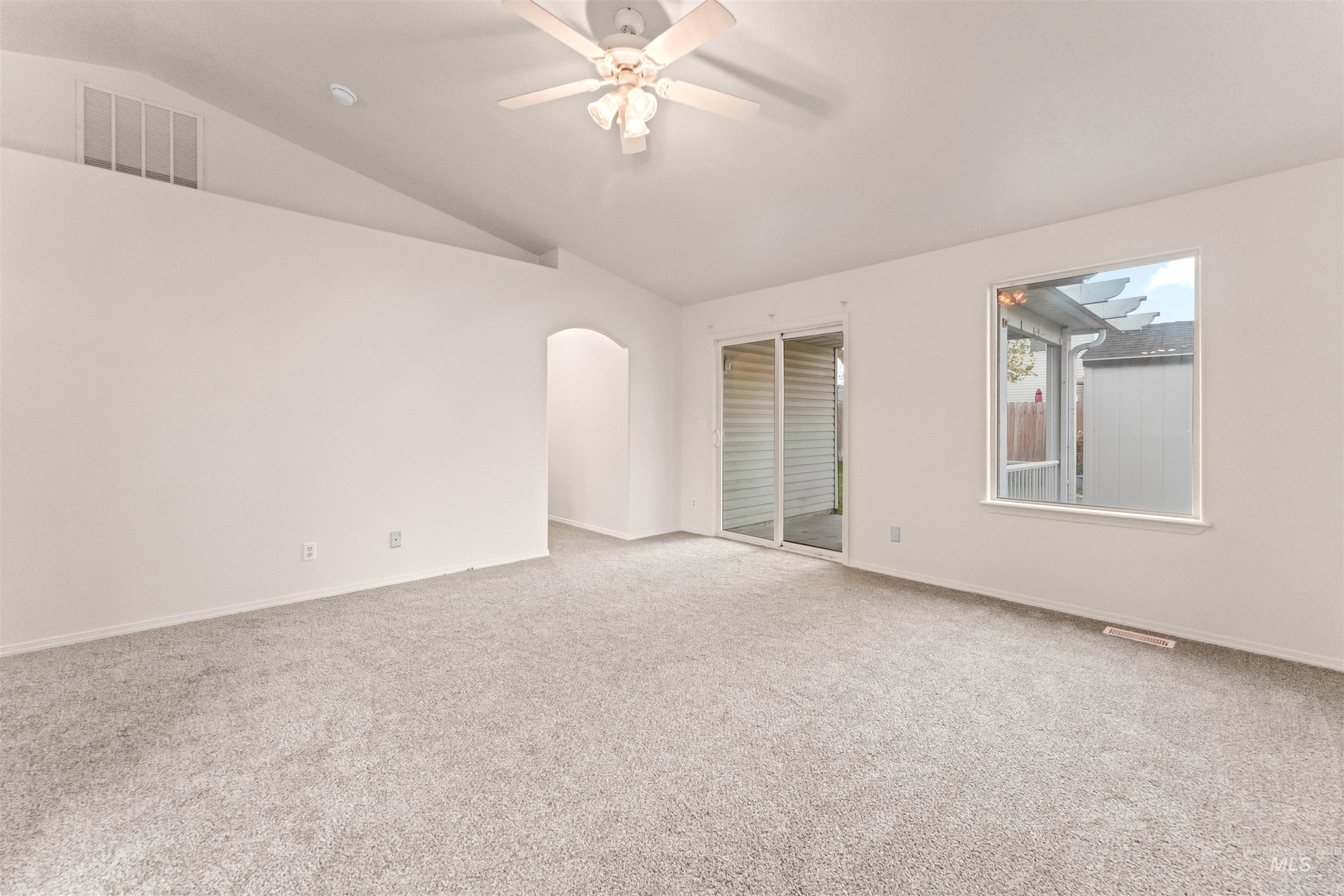 Empty room featuring vaulted ceiling, light carpet, ceiling fan, and arched walkways