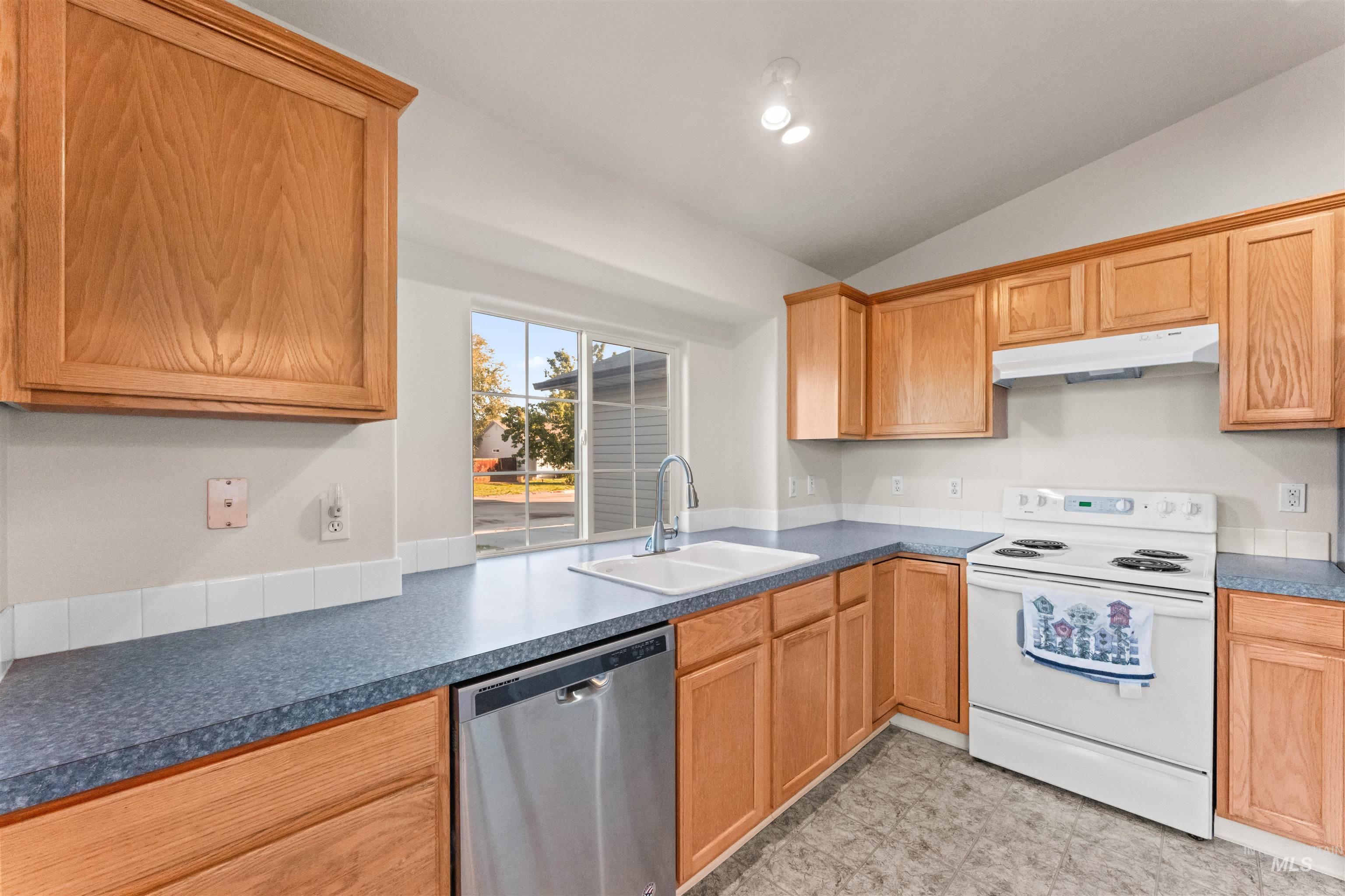 Kitchen with white electric range oven, stainless steel dishwasher, lofted ceiling, under cabinet range hood, and recessed lighting