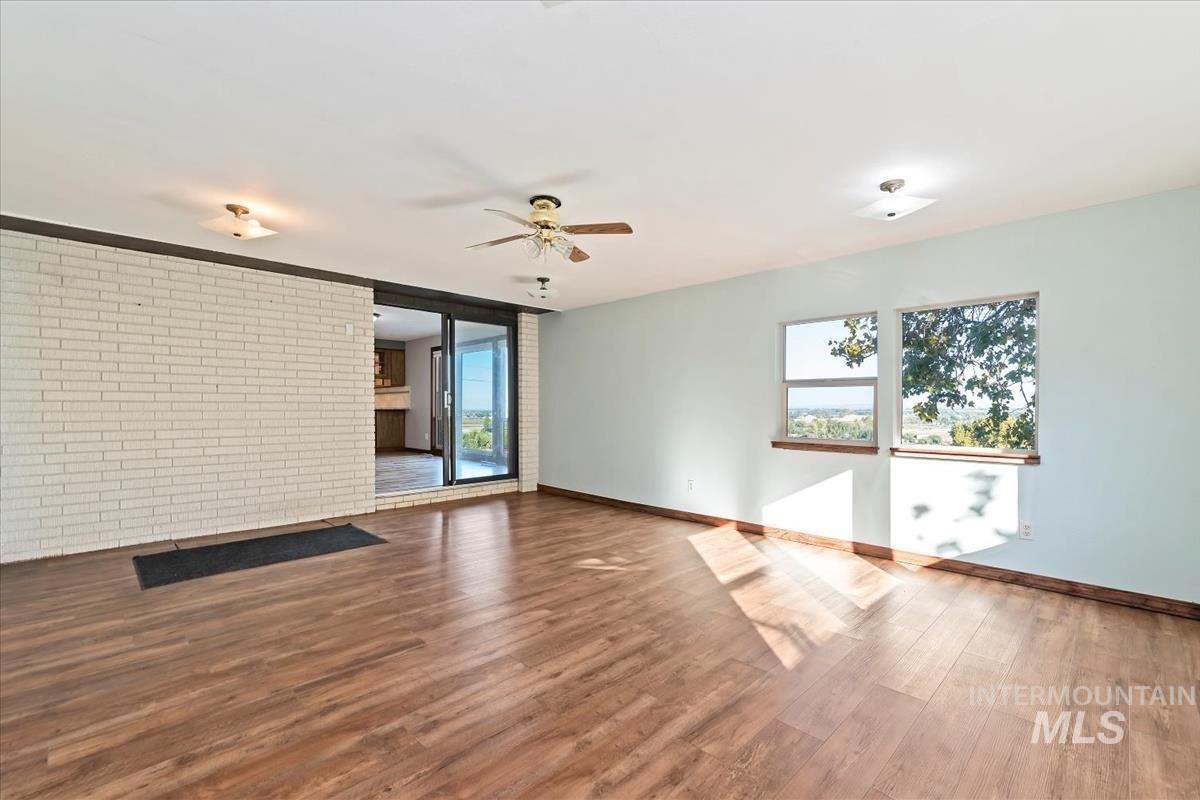Unfurnished living room featuring brick wall, dark wood-type flooring, and a ceiling fan