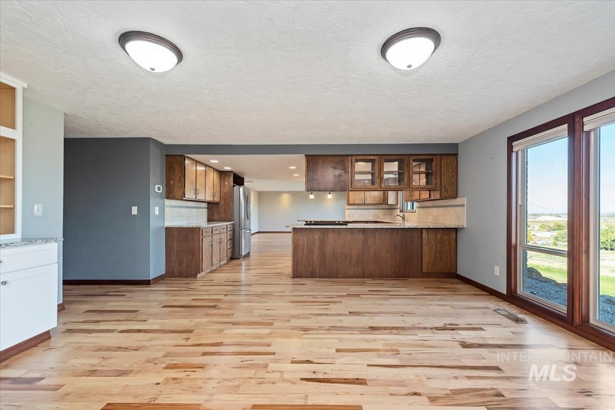 Kitchen with glass insert cabinets, a peninsula, light wood finished floors, brown cabinetry, and backsplash