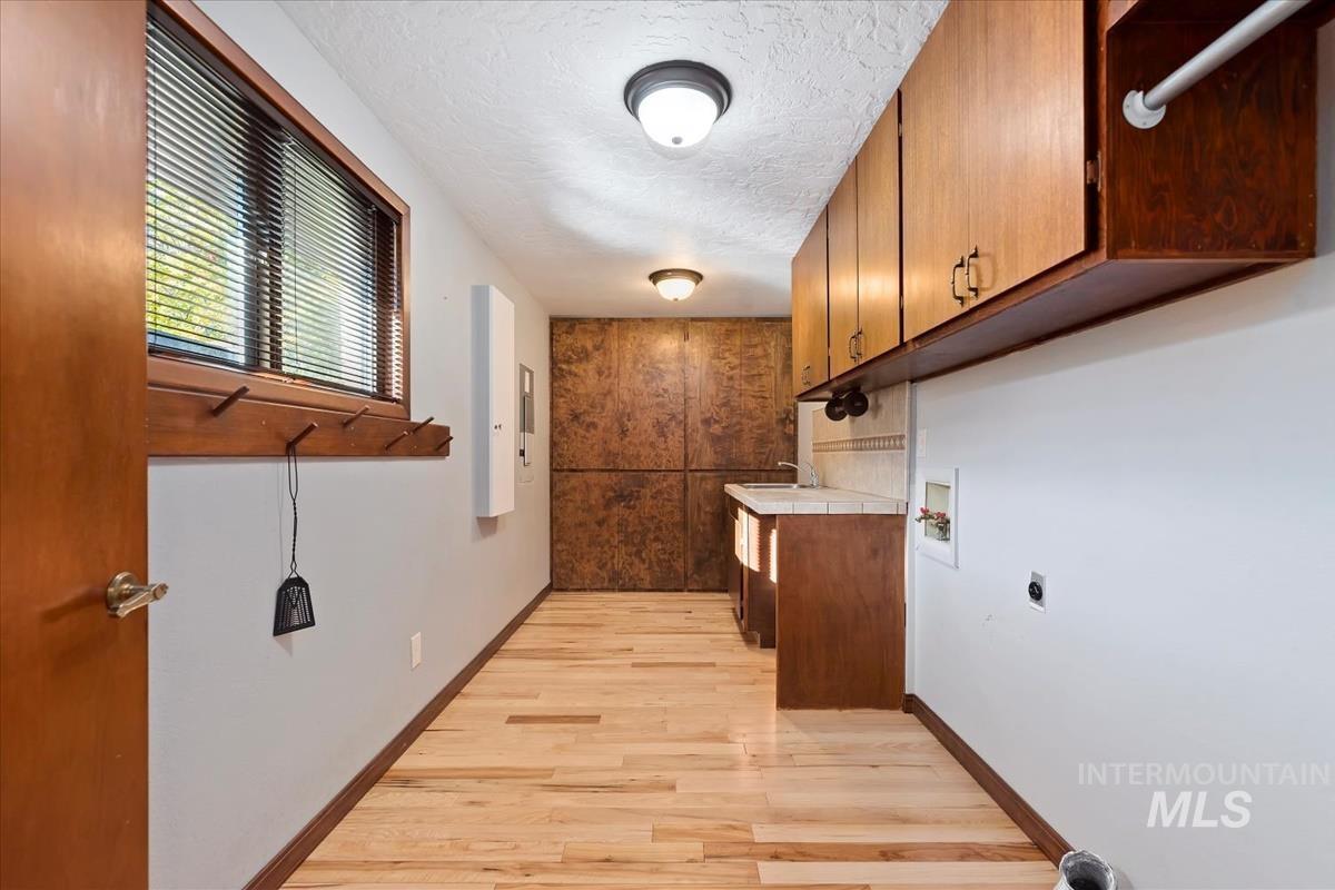 Washroom with a textured ceiling, light wood-style floors, cabinet space, electric dryer hookup, and washer hookup