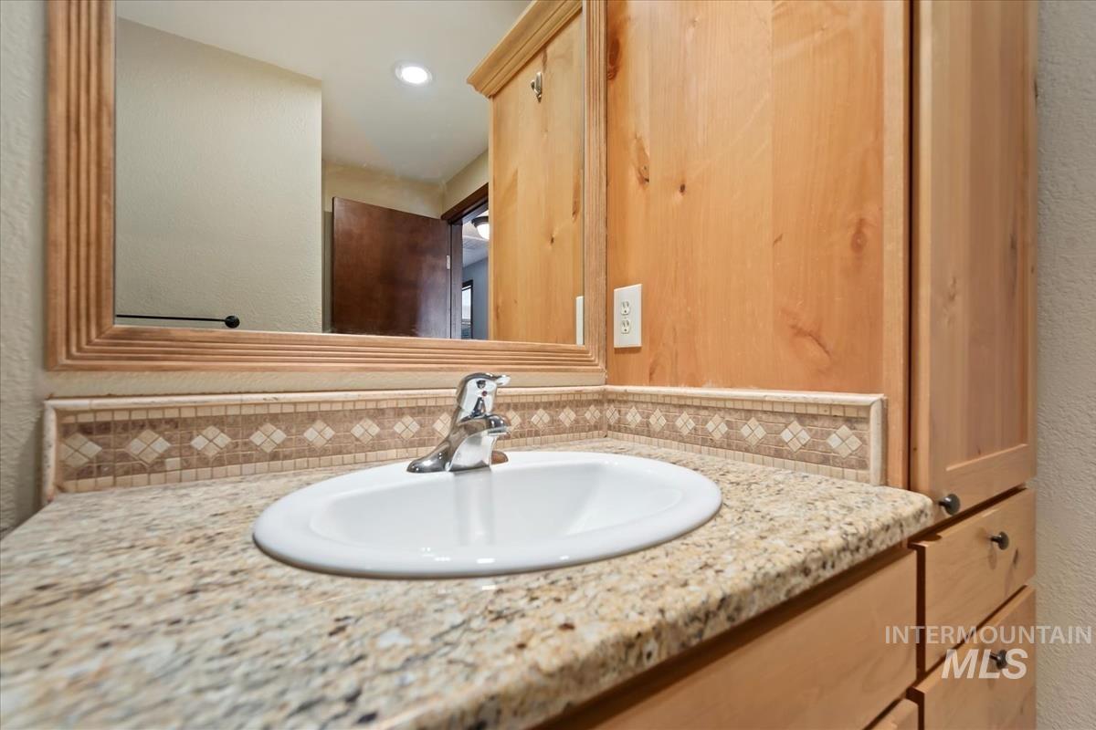 Bathroom featuring vanity, a textured wall, backsplash, and recessed lighting