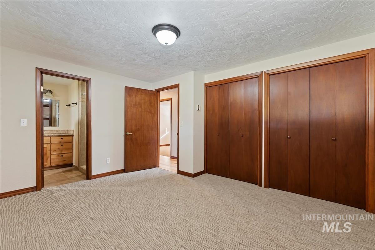 Unfurnished bedroom with carpet, two closets, a textured ceiling, and ensuite bathroom