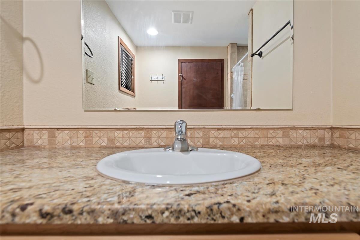 Bathroom view of vanity, a textured wall, curtained shower, and decorative backsplash