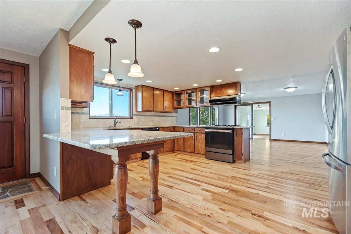 Kitchen featuring a peninsula, brown cabinets, glass insert cabinets, decorative light fixtures, and recessed lighting