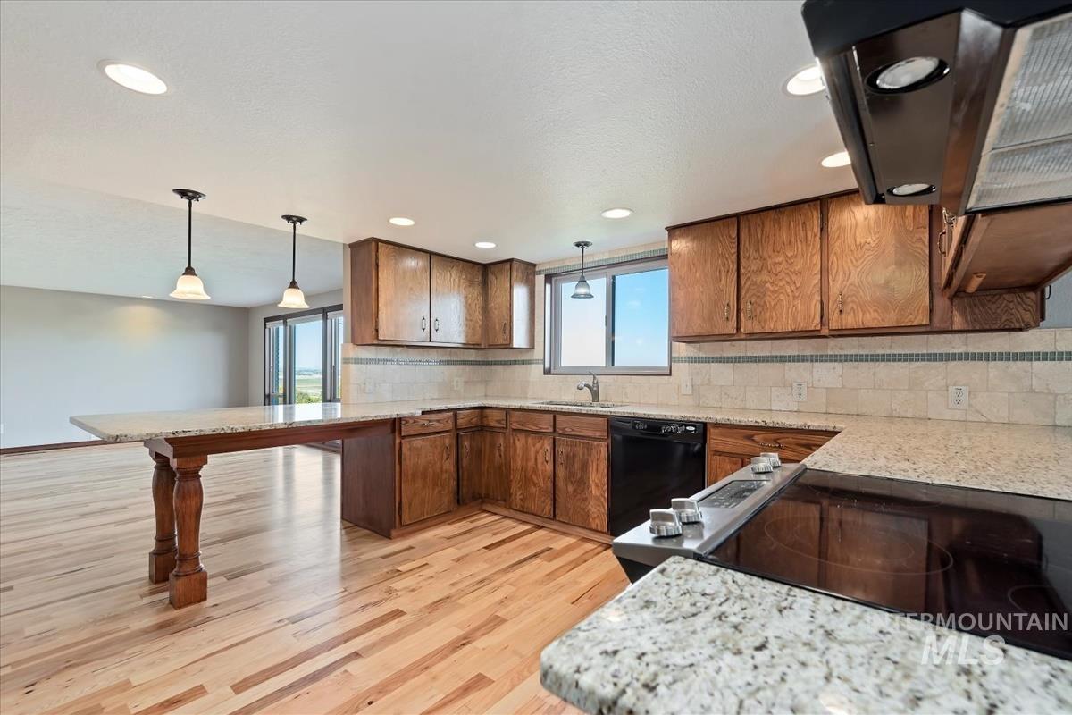 Kitchen with tasteful backsplash, range hood, decorative light fixtures, light wood-style flooring, and light stone counters