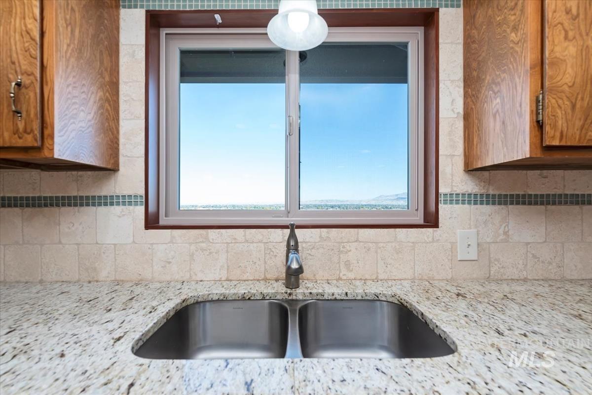 Kitchen with brown cabinets, decorative backsplash, light stone counters, and plenty of natural light