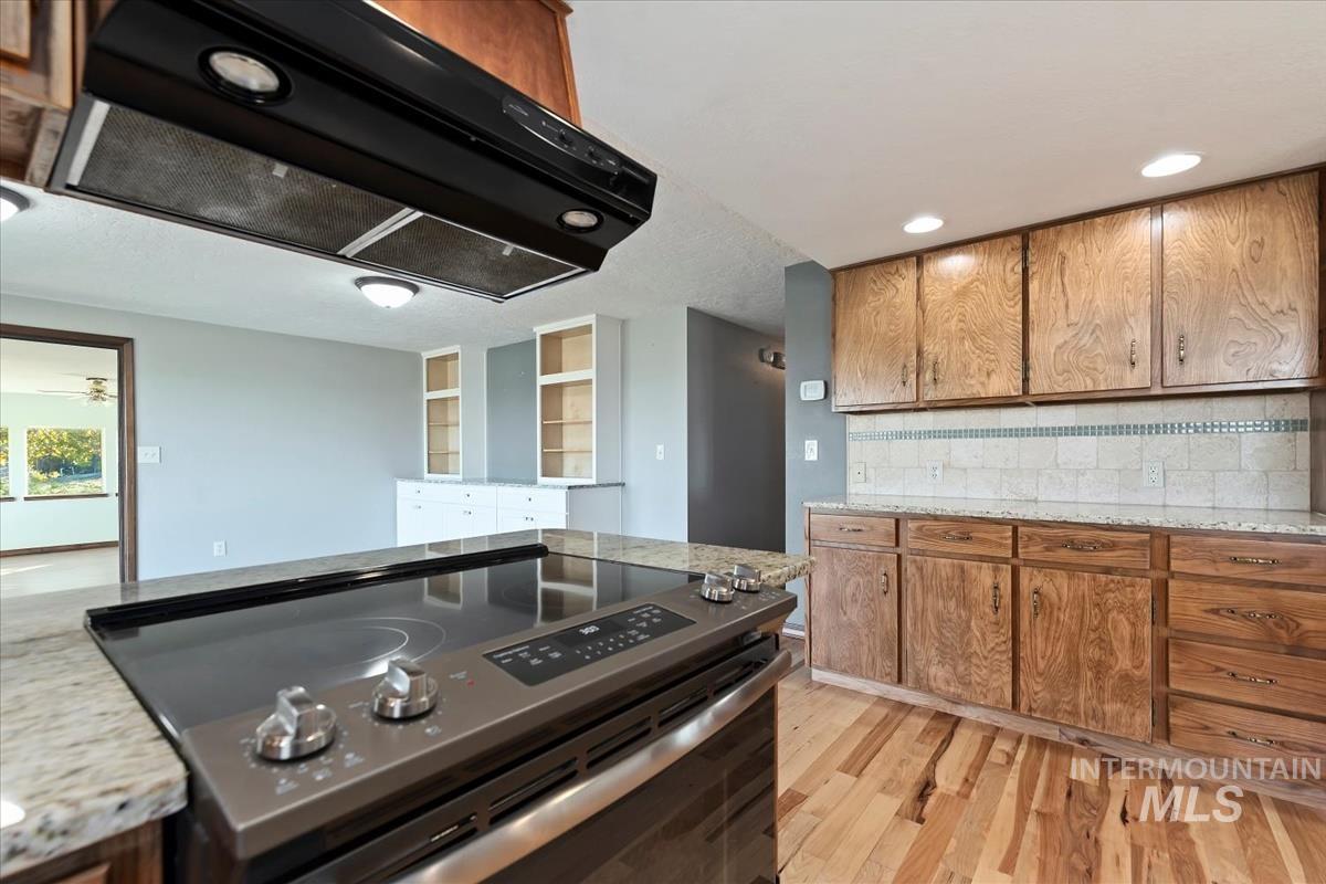 Kitchen with range hood, brown cabinetry, electric range, light stone countertops, and recessed lighting