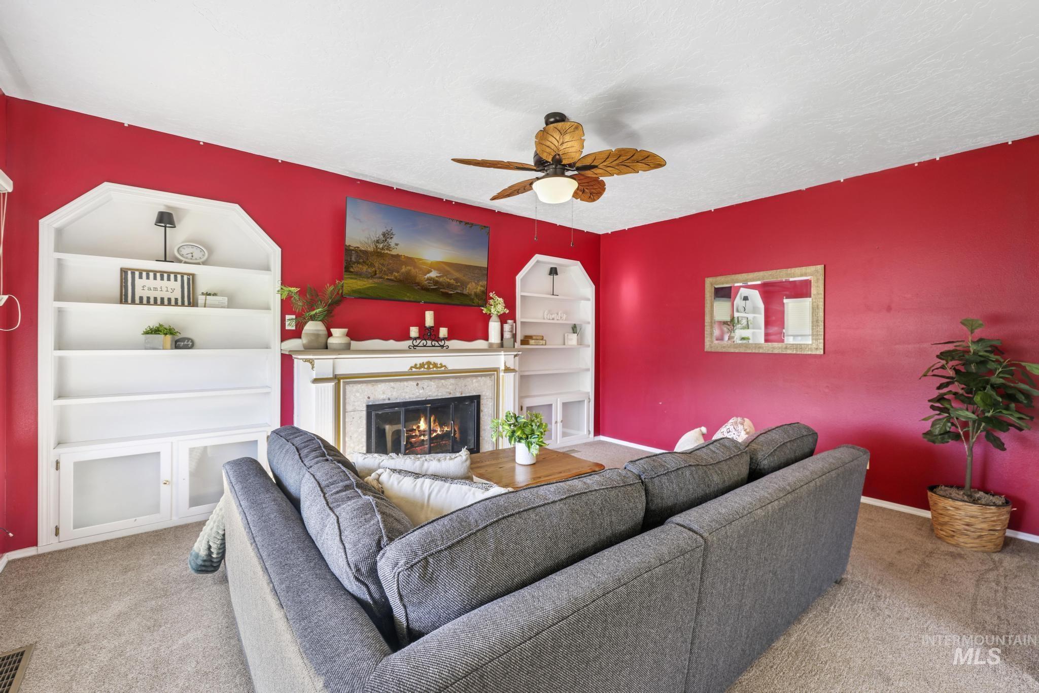 Living area with carpet, a tiled fireplace, built in shelves, a ceiling fan, and a textured ceiling