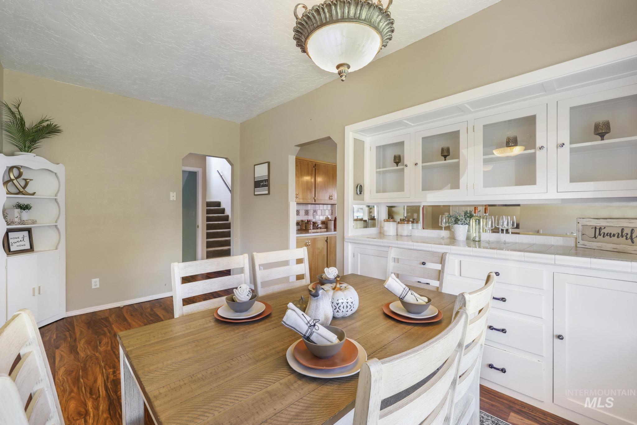 Dining area with a textured ceiling, arched walkways, dark wood-type flooring, and stairs